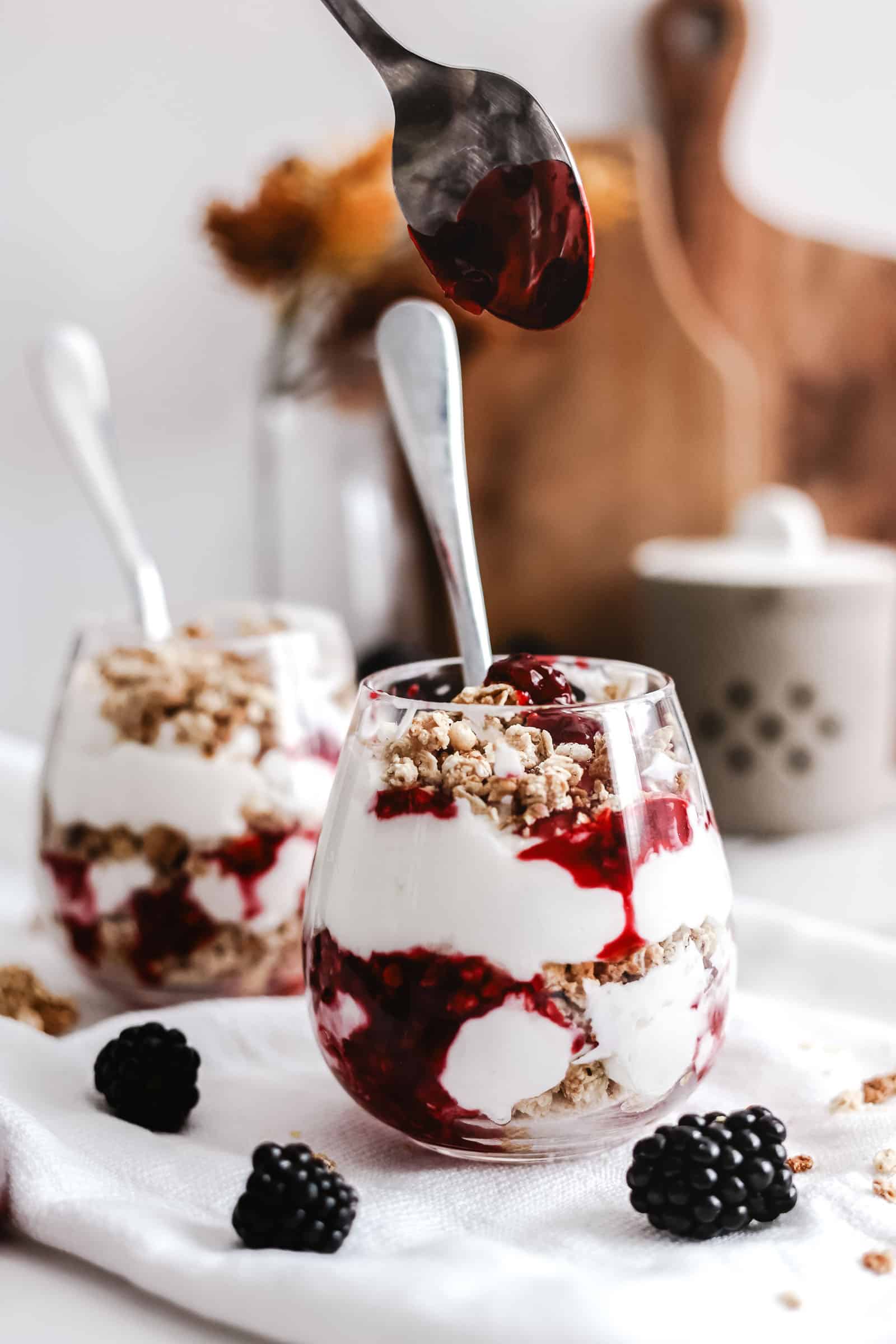 Blackberry compote being added to the top of a parfait.