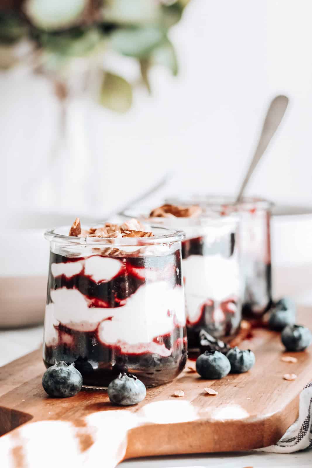 Three blueberry parfaits served on a wood board. 