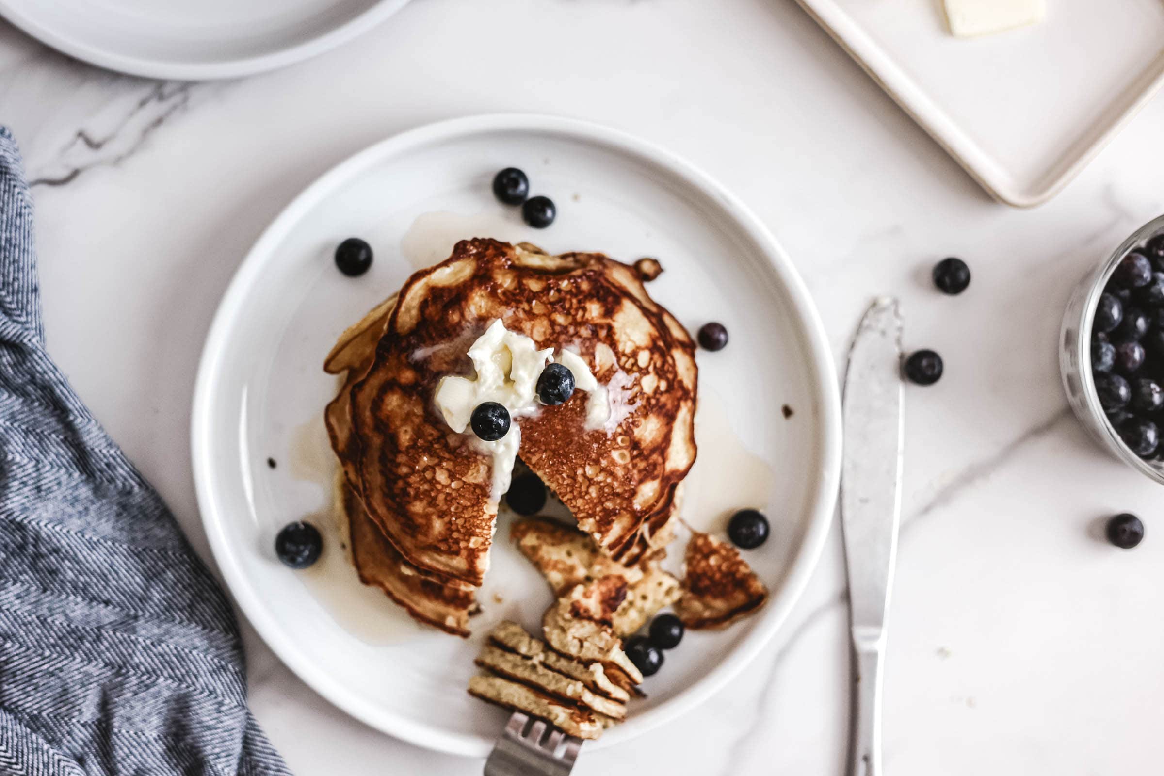 Pancakes on plate topped with butter and blueberries.