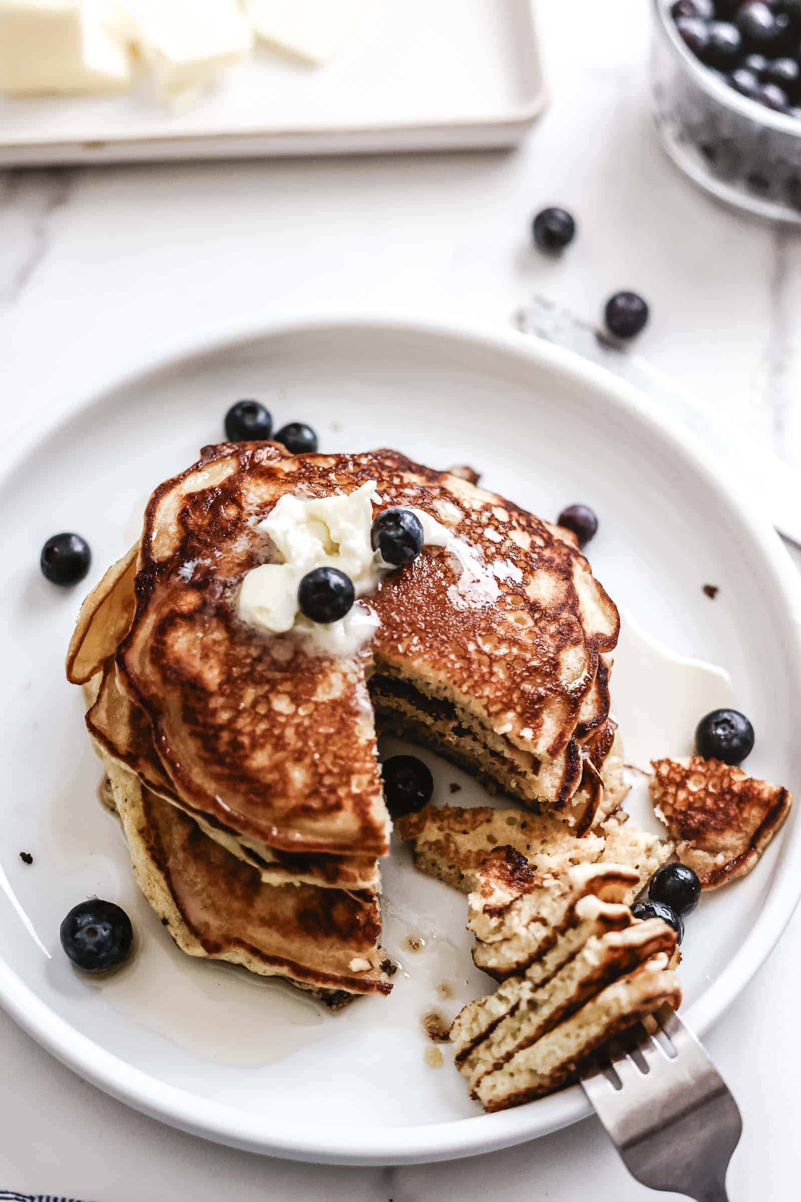 Pancakes on plate topped with butter and blueberries.