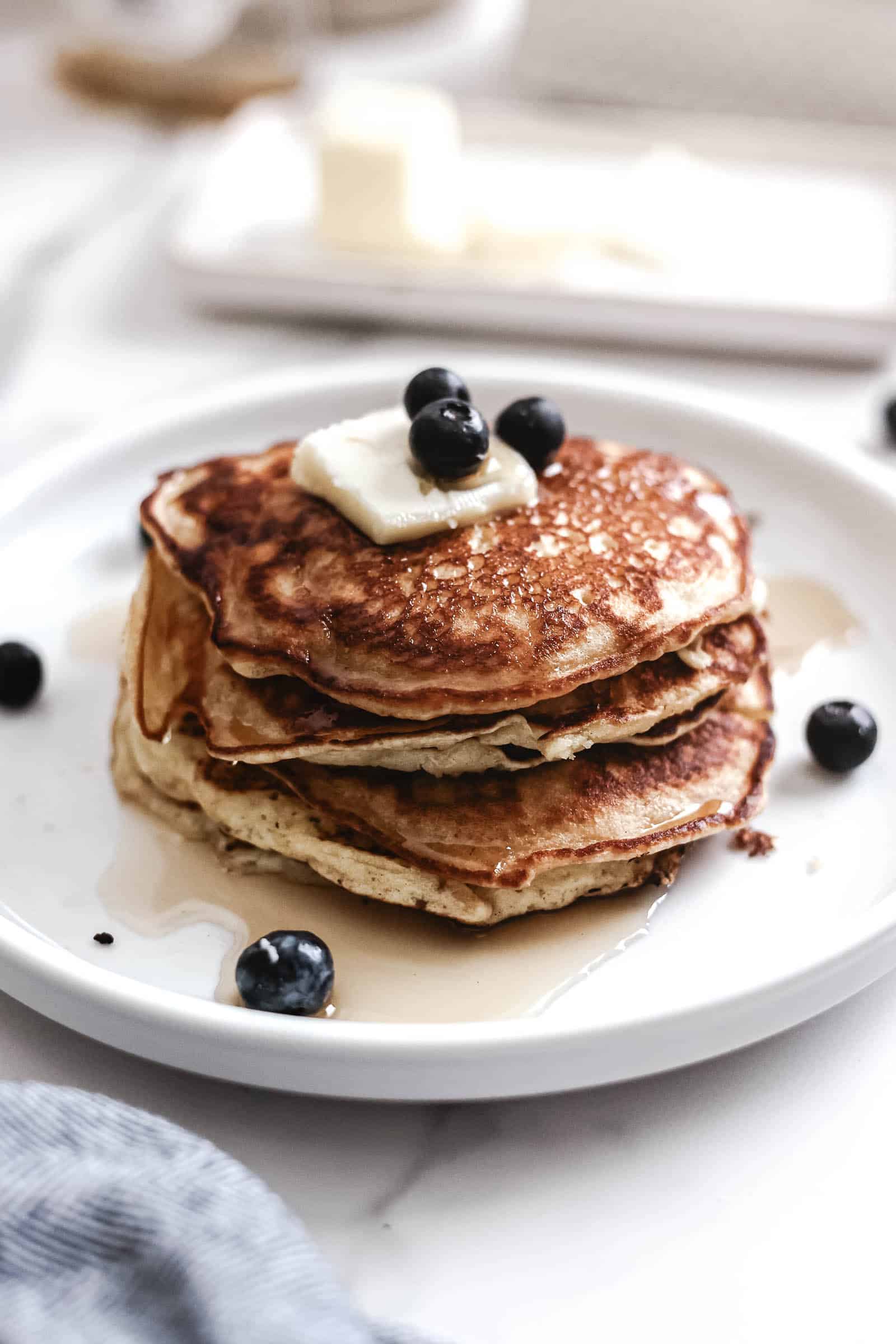 Pancakes on plate topped with butter and blueberries.