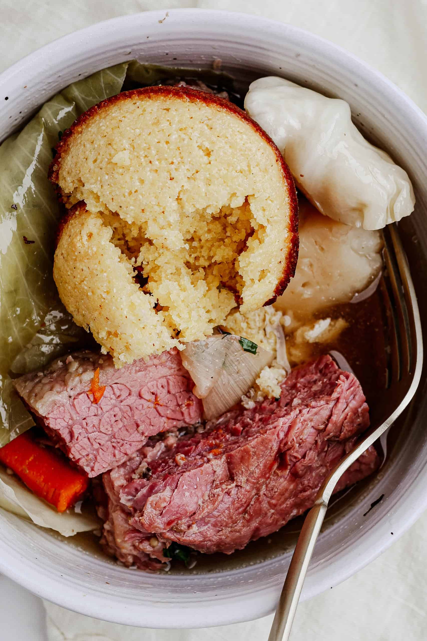 Corned beef topped with a cornbread muffin served in a bowl.
