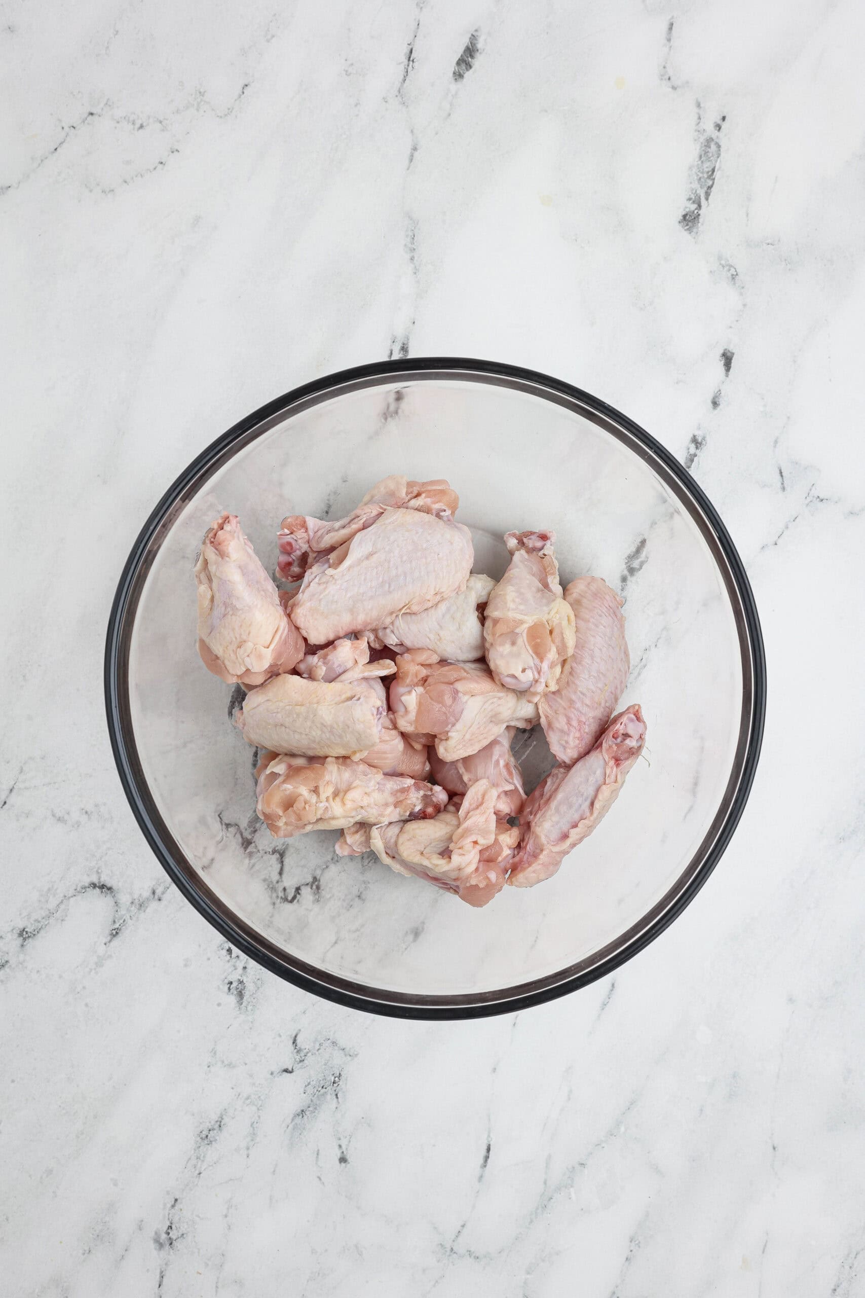 Raw chicken wings in a glass mixing bowl before seasoning.