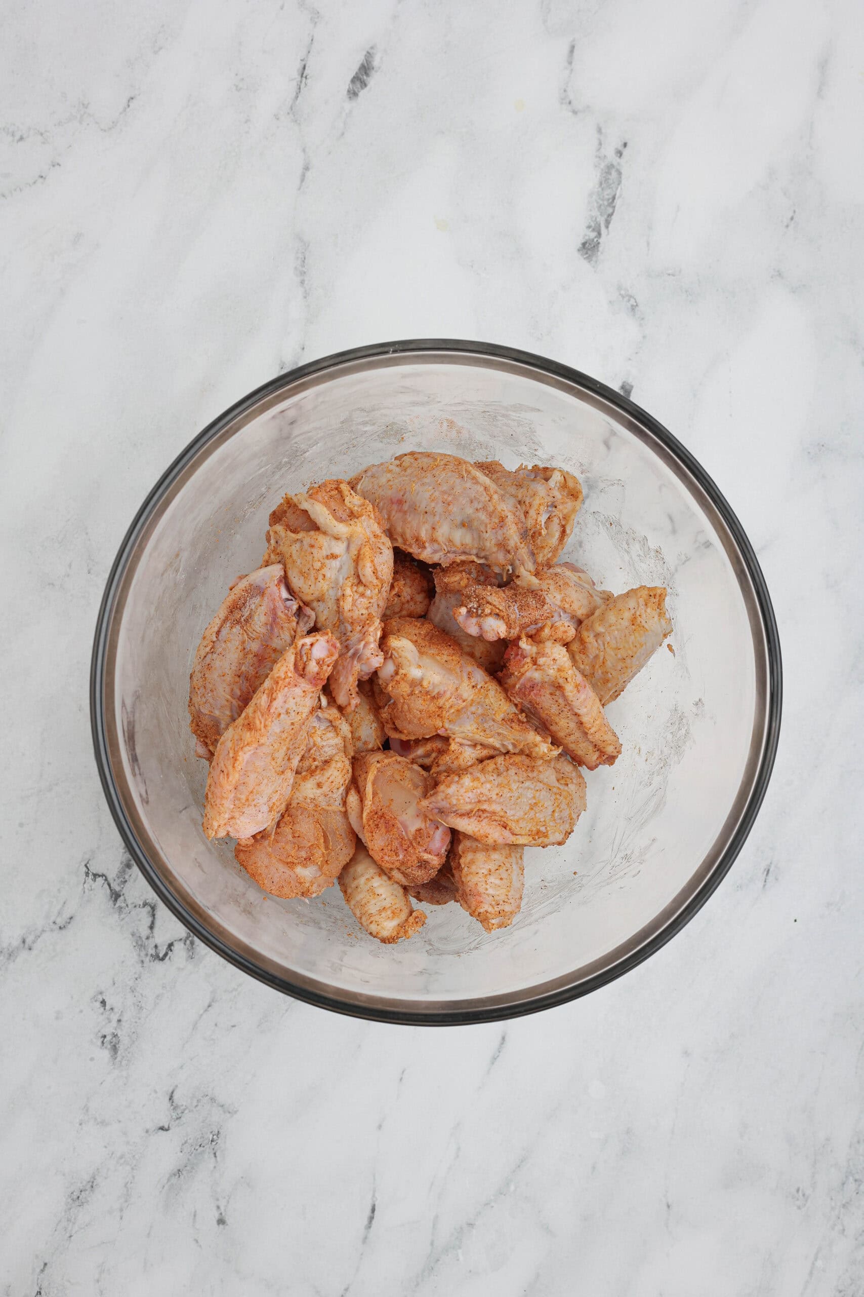 Chicken wings coated with dry rub seasonings in a mixing bowl, ready for baking.