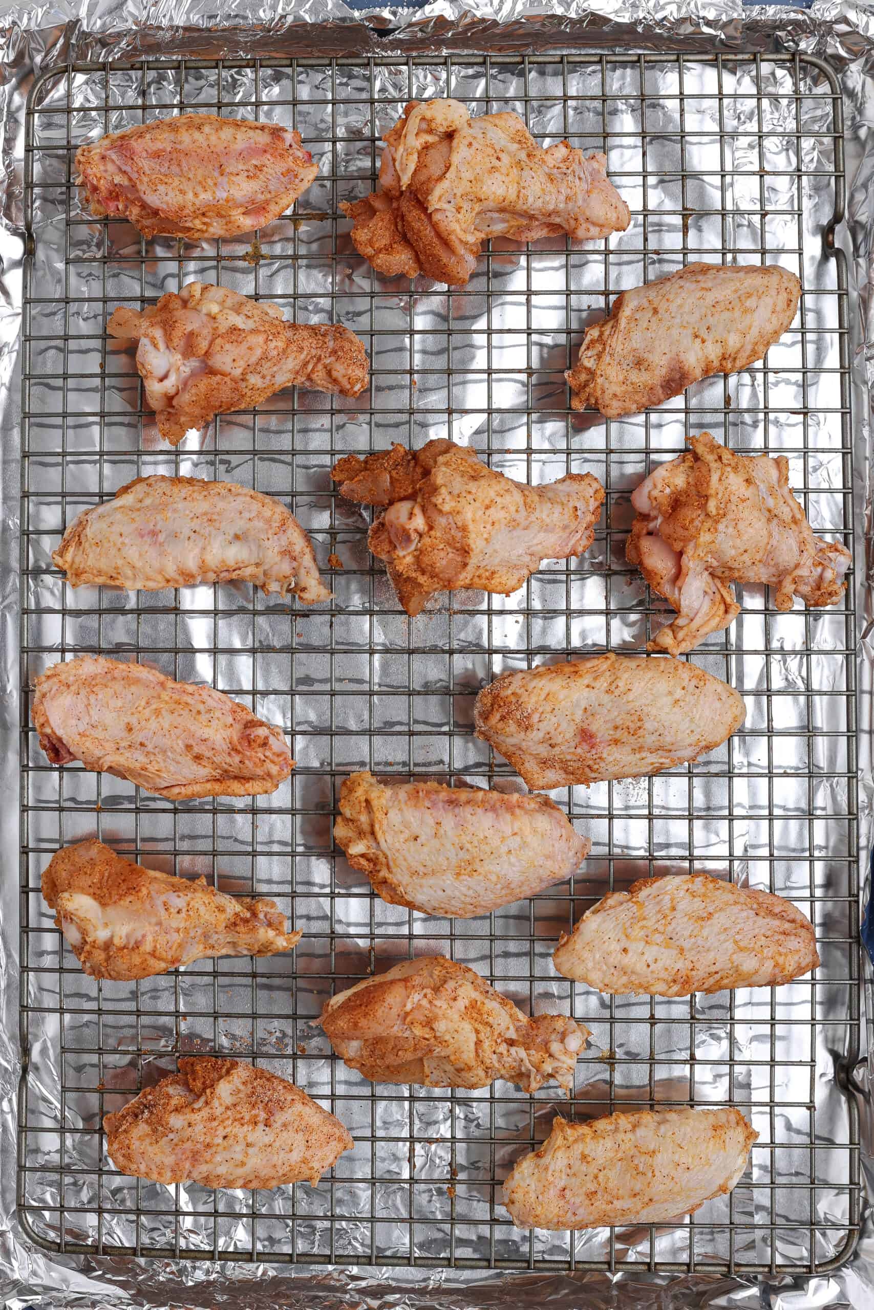 Seasoned chicken wings arranged on a wire rack over a foil-lined baking sheet, ready to go into the oven.