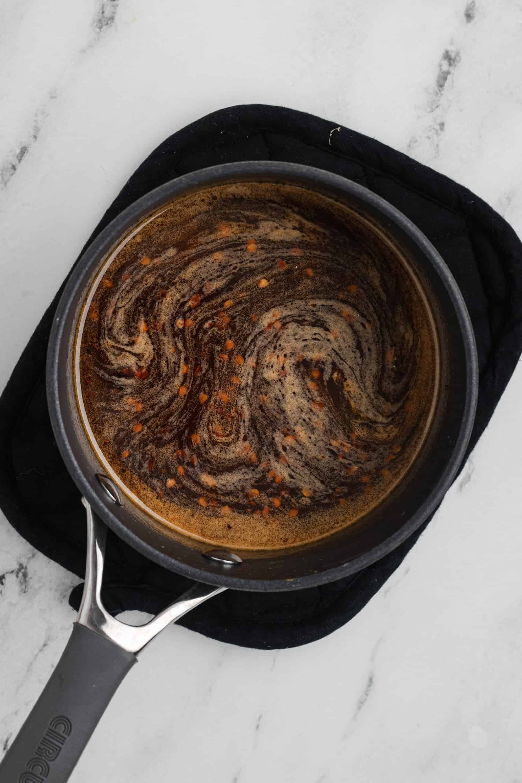 Small saucepan with melted butter, honey, and hot sauce being mixed together to make the hot honey glaze.