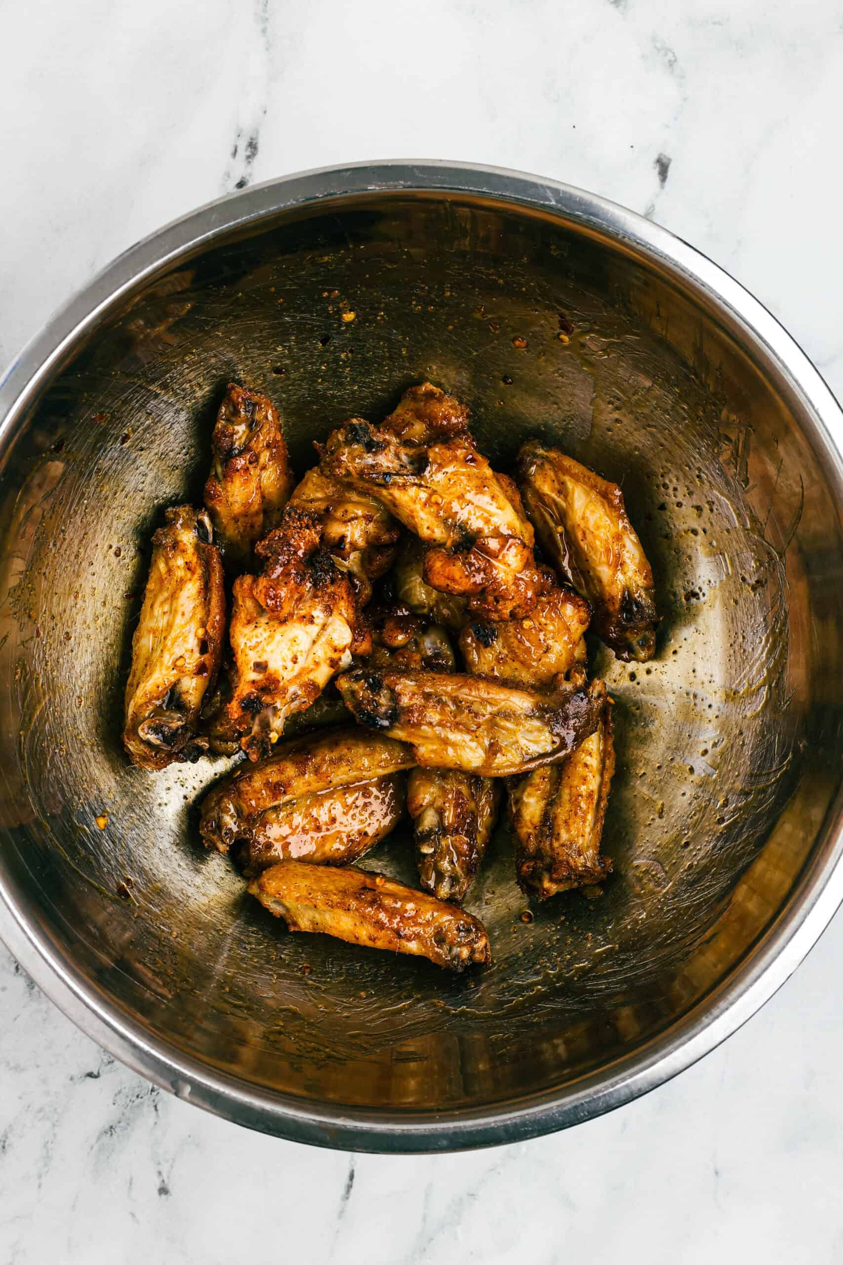 Cooked chicken wings in a stainless steel bowl being tossed in hot honey sauce.