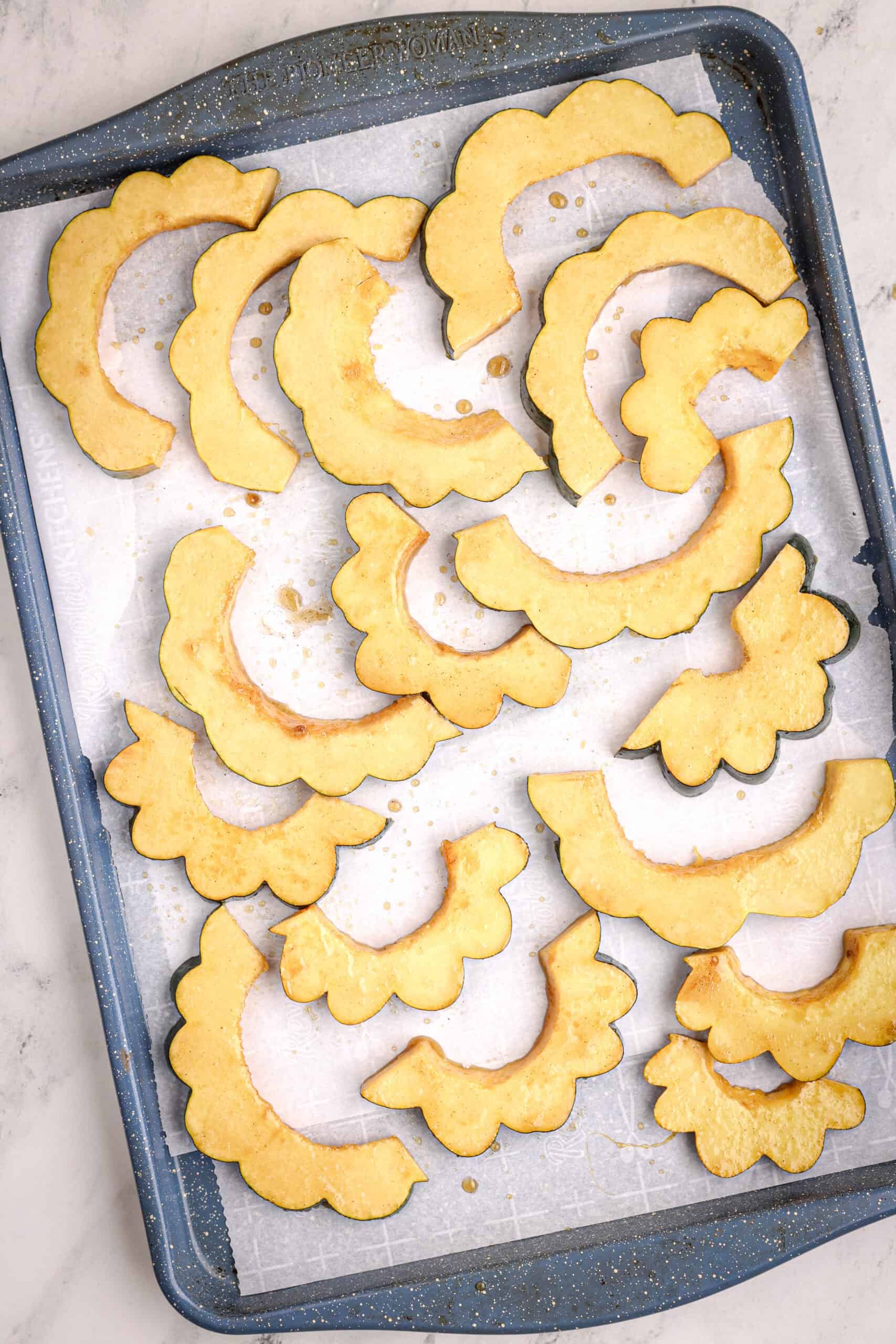 Uncooked maple-coated acorn squash slices arranged in a single layer on a parchment-lined baking sheet.