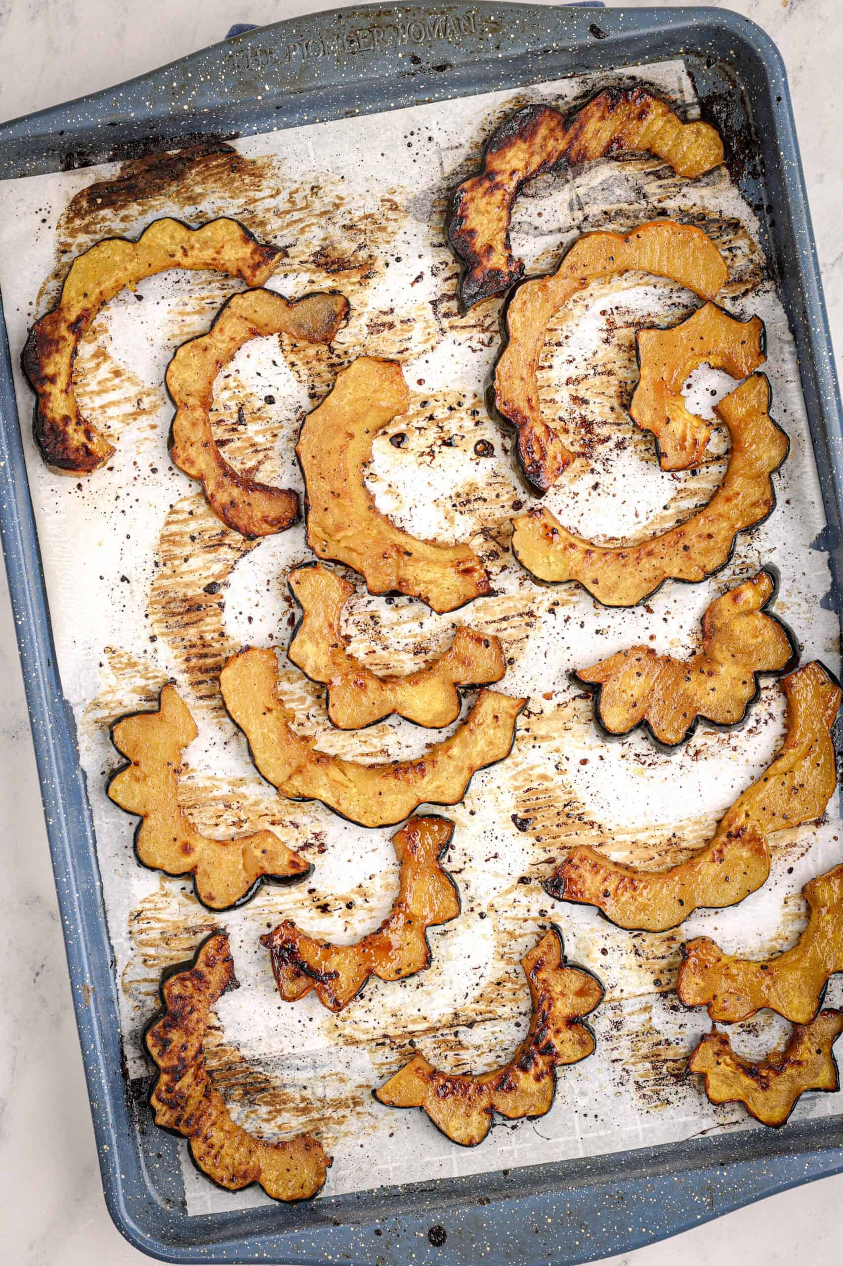 oasted acorn squash slices on a parchment-lined baking sheet, showing caramelized edges and golden centers.