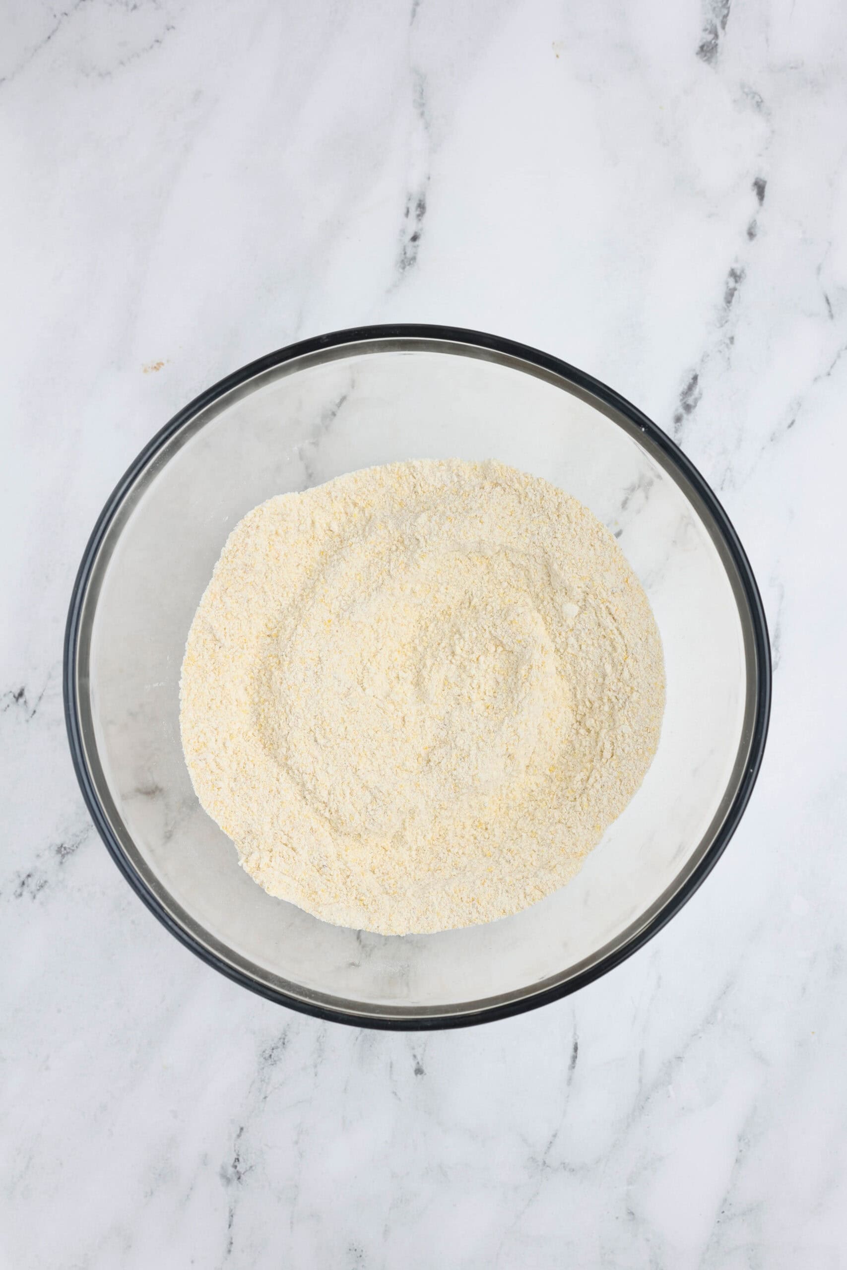 Glass mixing bowl filled with dry ingredients—cornmeal, flour, sugar, baking powder, and salt—ready to be combined for cornbread batter.