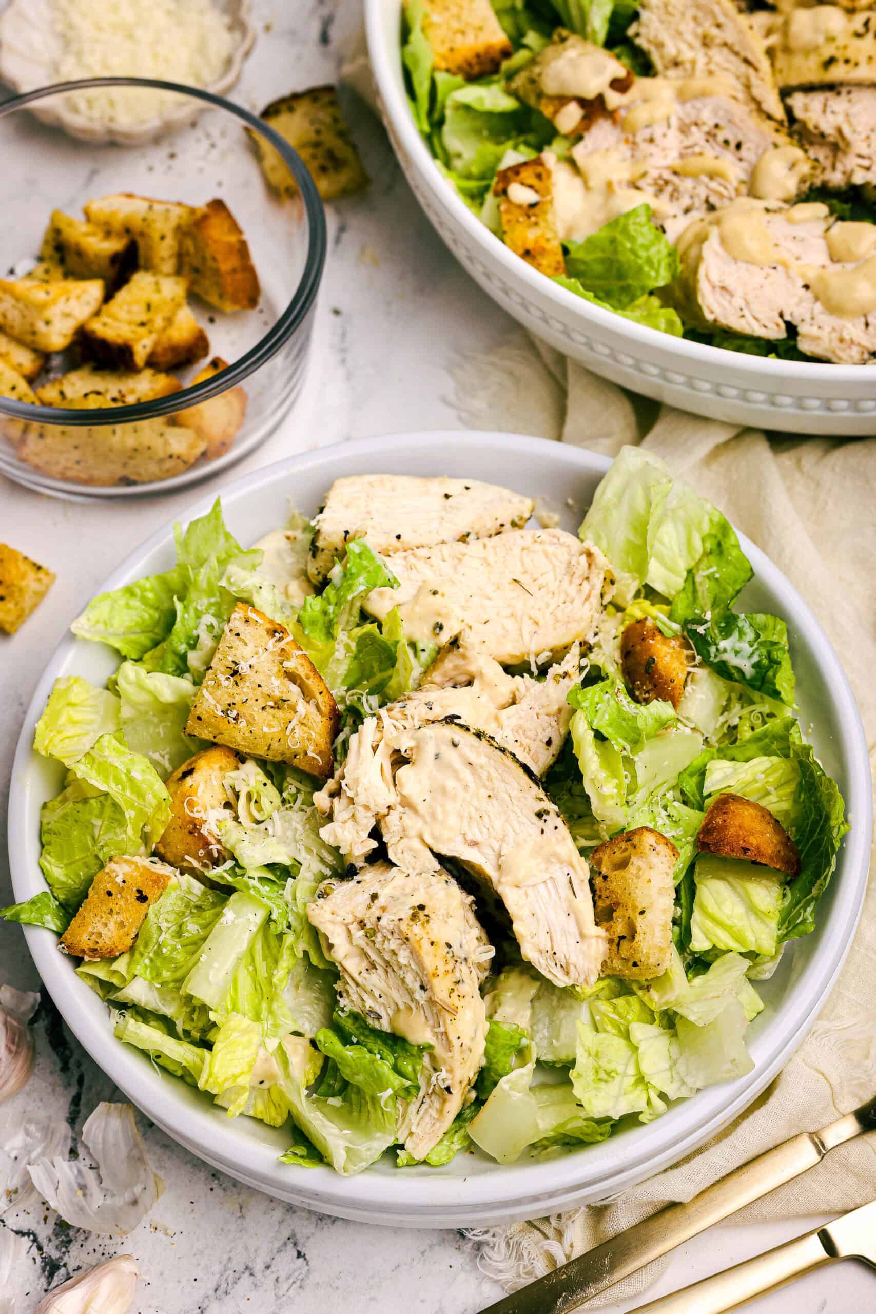 Overhead view of homemade chicken Caesar salad topped with grilled chicken, golden garlic croutons, and shaved Parmesan cheese