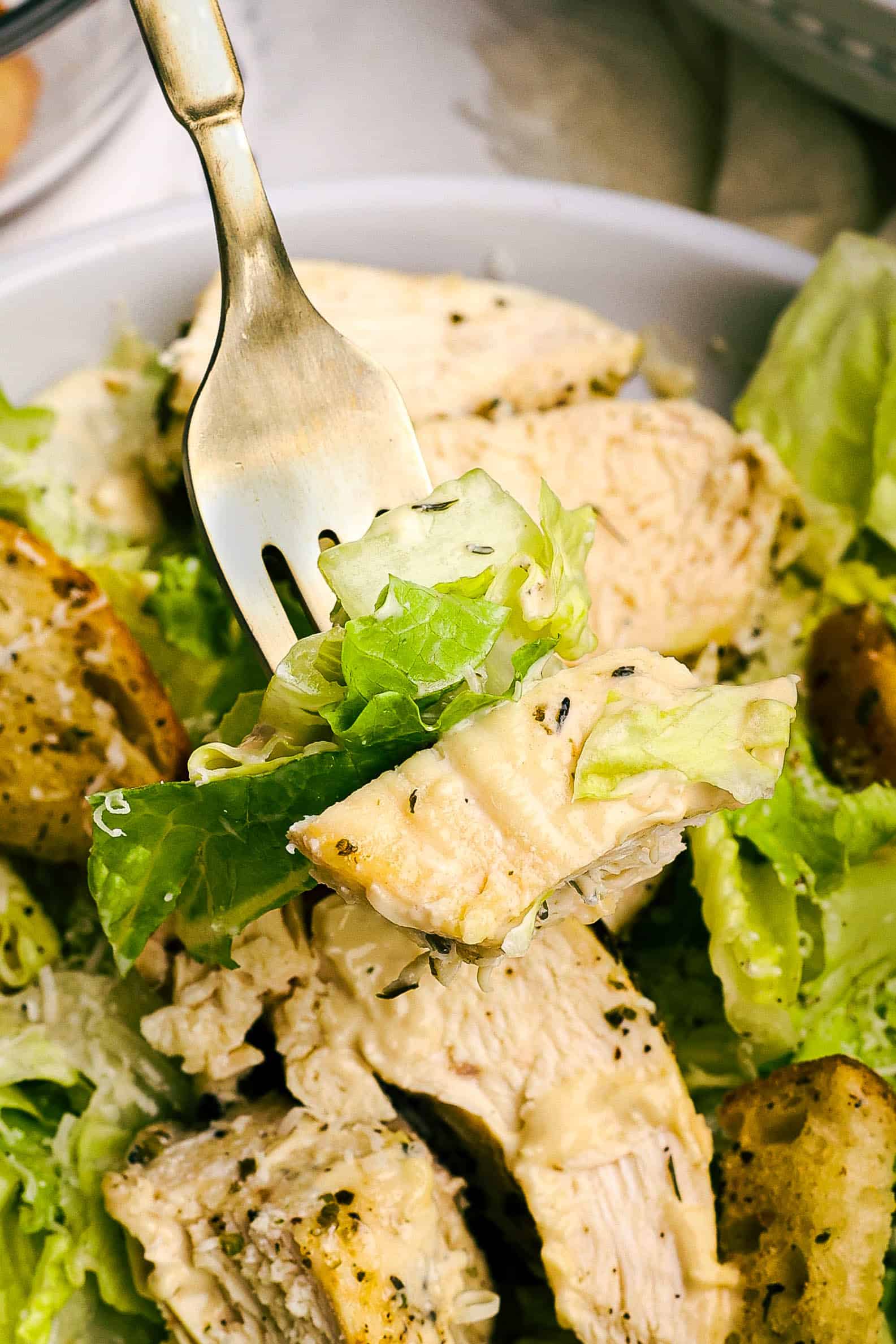 Fork lifting a bite of chicken Caesar salad with romaine lettuce, tender chicken, and creamy Caesar dressing