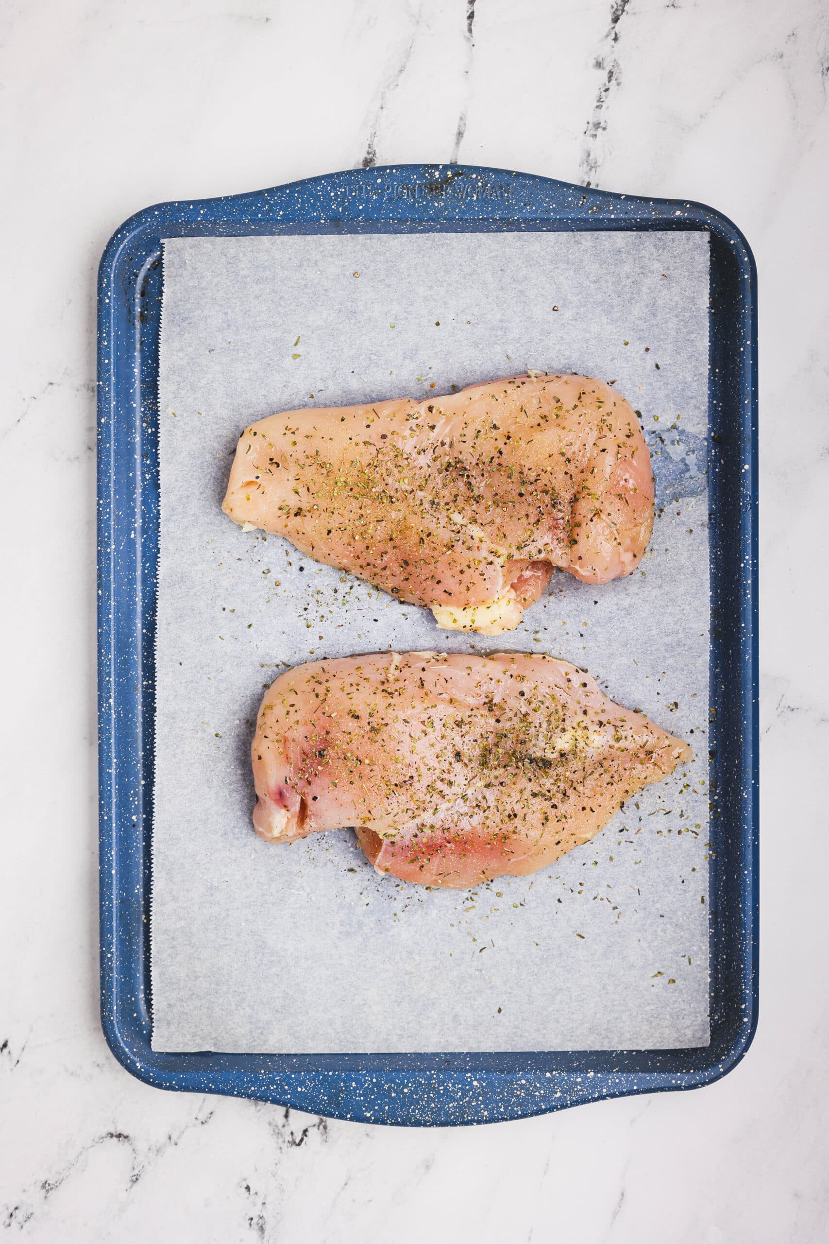 Raw chicken breasts seasoned with herbs and spices on a parchment-lined baking sheet
