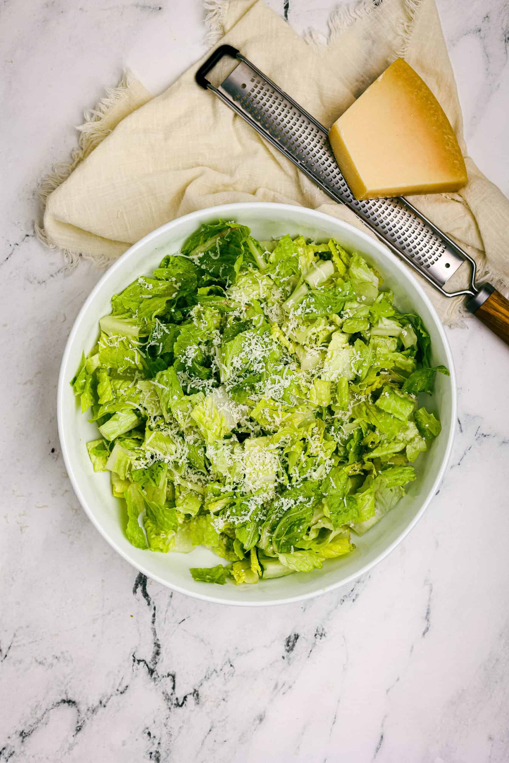 Bowl of chopped romaine lettuce tossed with grated Parmesan cheese for Caesar salad