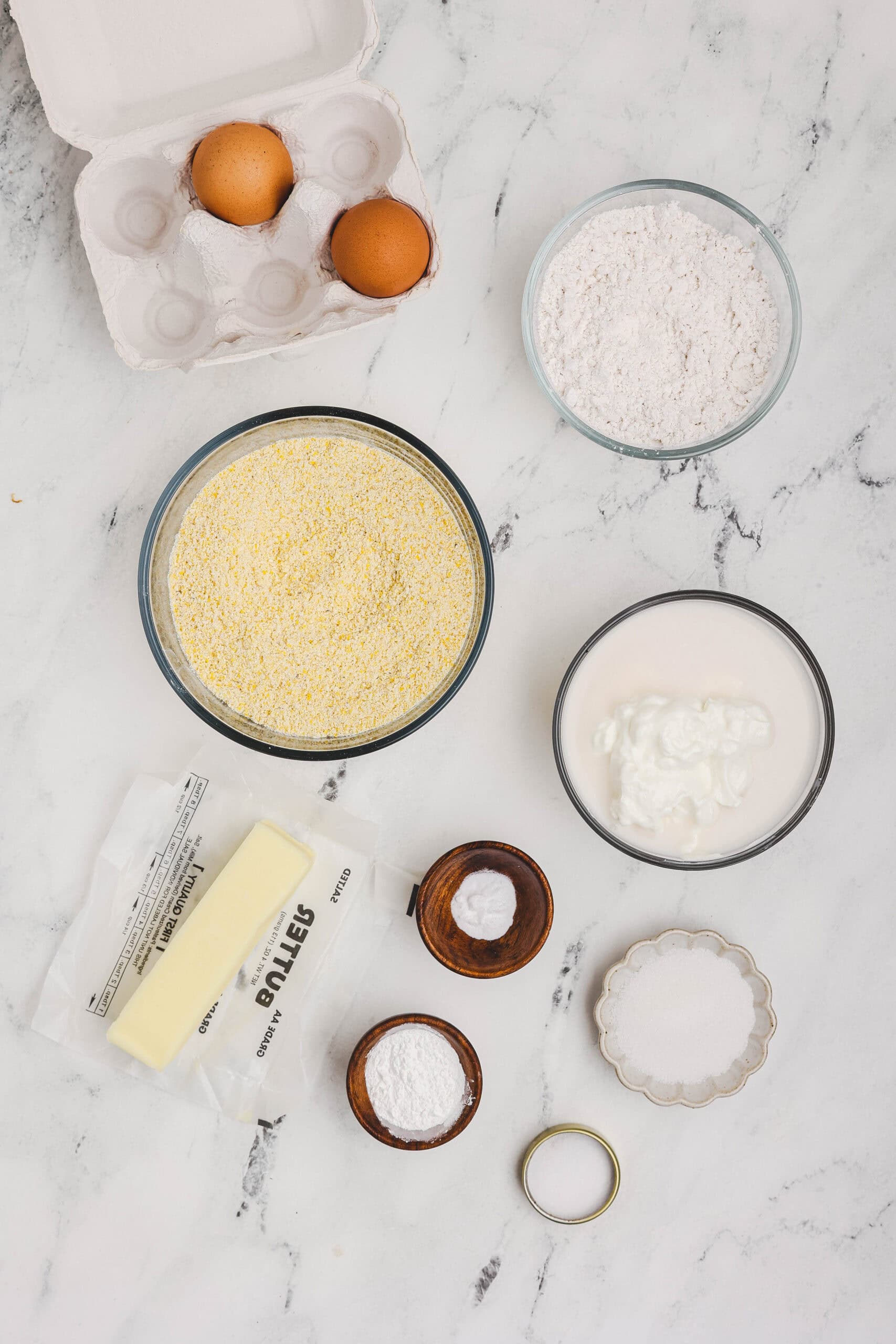 Ingredients for homemade cast iron cornbread including cornmeal, flour, eggs, butter, milk, sour cream, and baking powder.