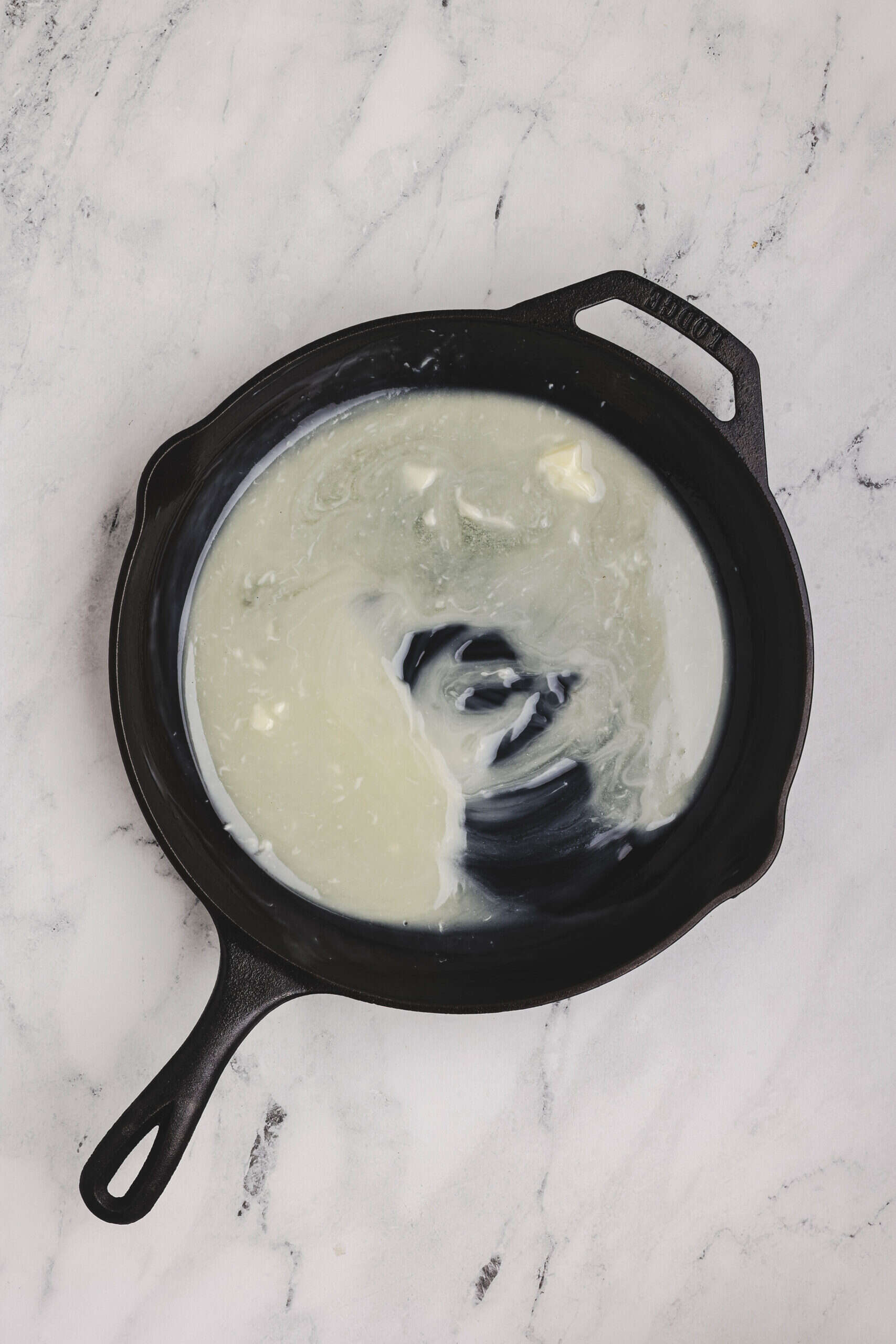 Melted butter swirling in a hot cast iron skillet before adding cornbread batter.