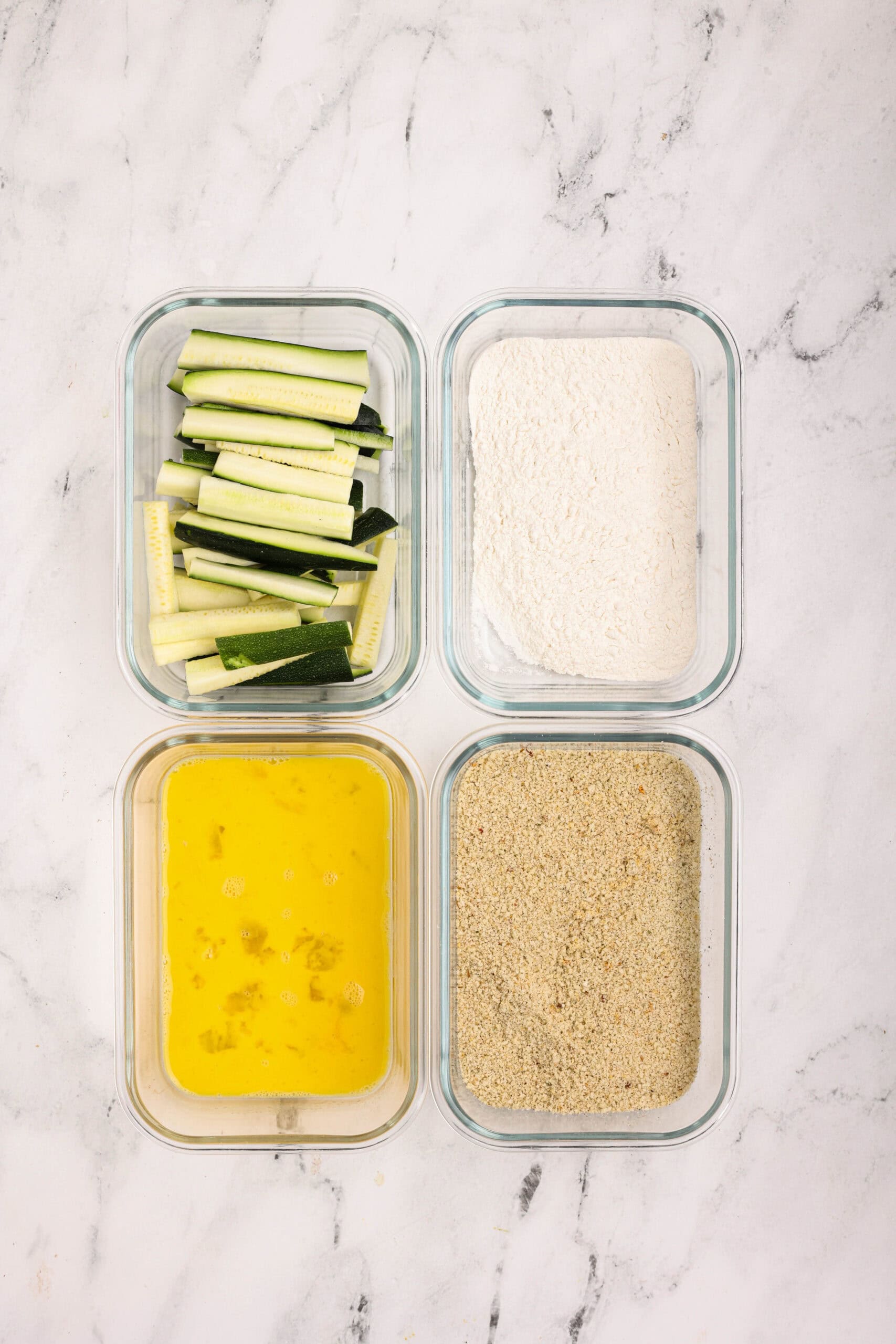 Breading station for zucchini fries with bowls of flour, beaten eggs, and blended breadcrumb mixture.