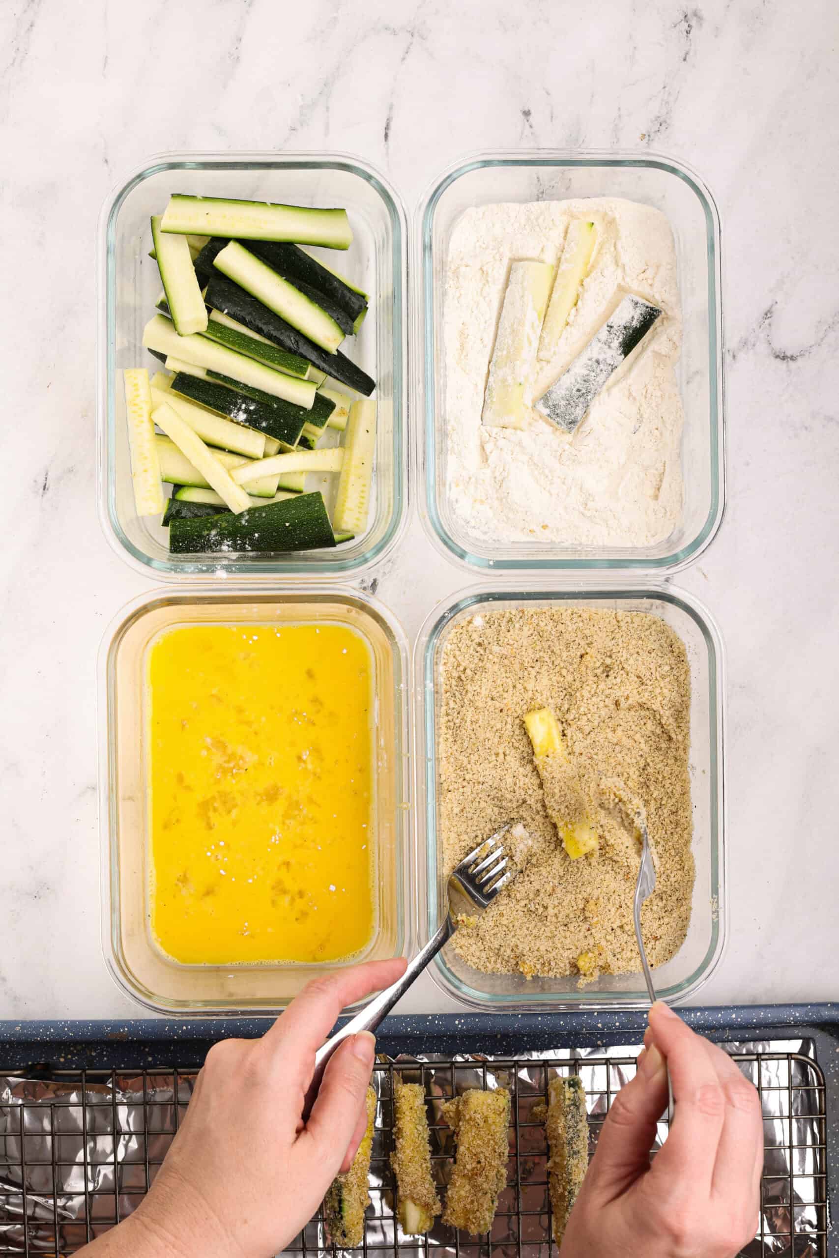 Hands breading zucchini sticks by dipping them into egg and breadcrumb mixture before baking.