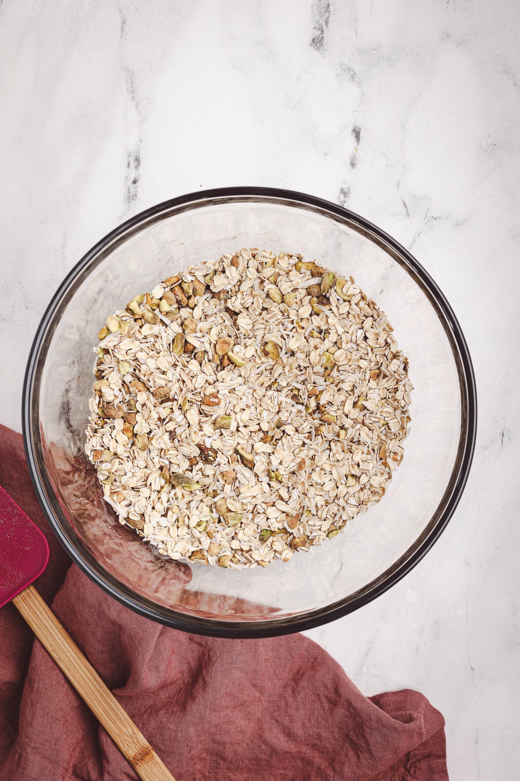 Rolled oats and chopped nuts in a glass mixing bowl prepared for homemade granola.