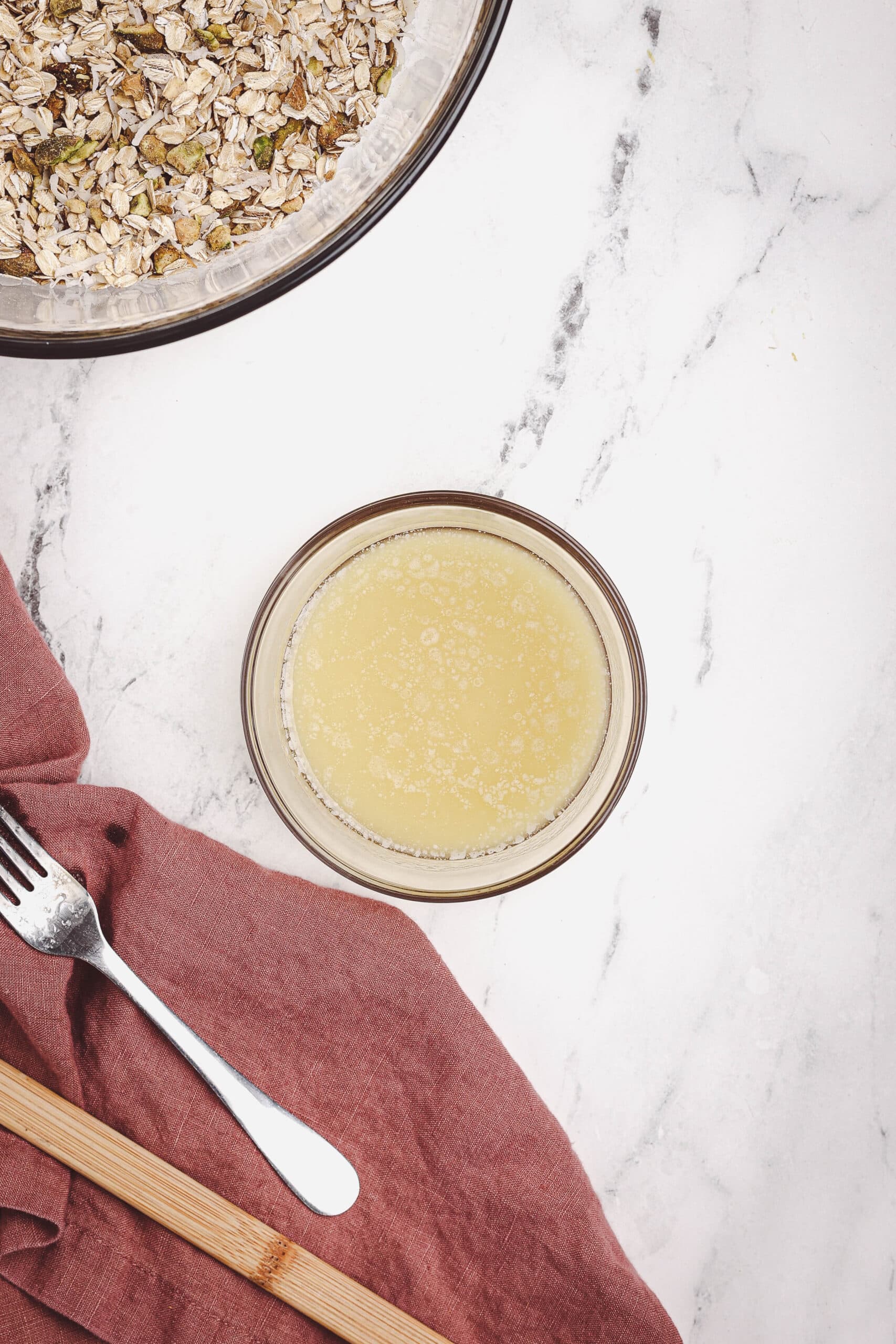 Melted butter mixture for granola in a glass bowl on a white countertop.