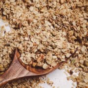 Homemade granola with rolled oats, toasted coconut, and chopped nuts served on a wooden spoon with a golden, crisp texture.
