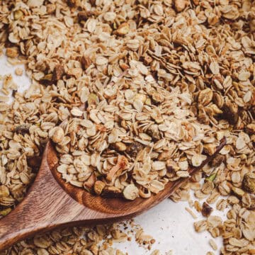 Homemade granola with rolled oats, toasted coconut, and chopped nuts served on a wooden spoon with a golden, crisp texture.