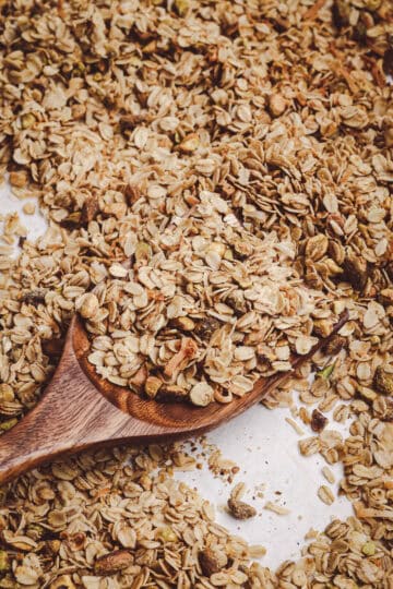 Homemade granola with rolled oats, toasted coconut, and chopped nuts served on a wooden spoon with a golden, crisp texture.