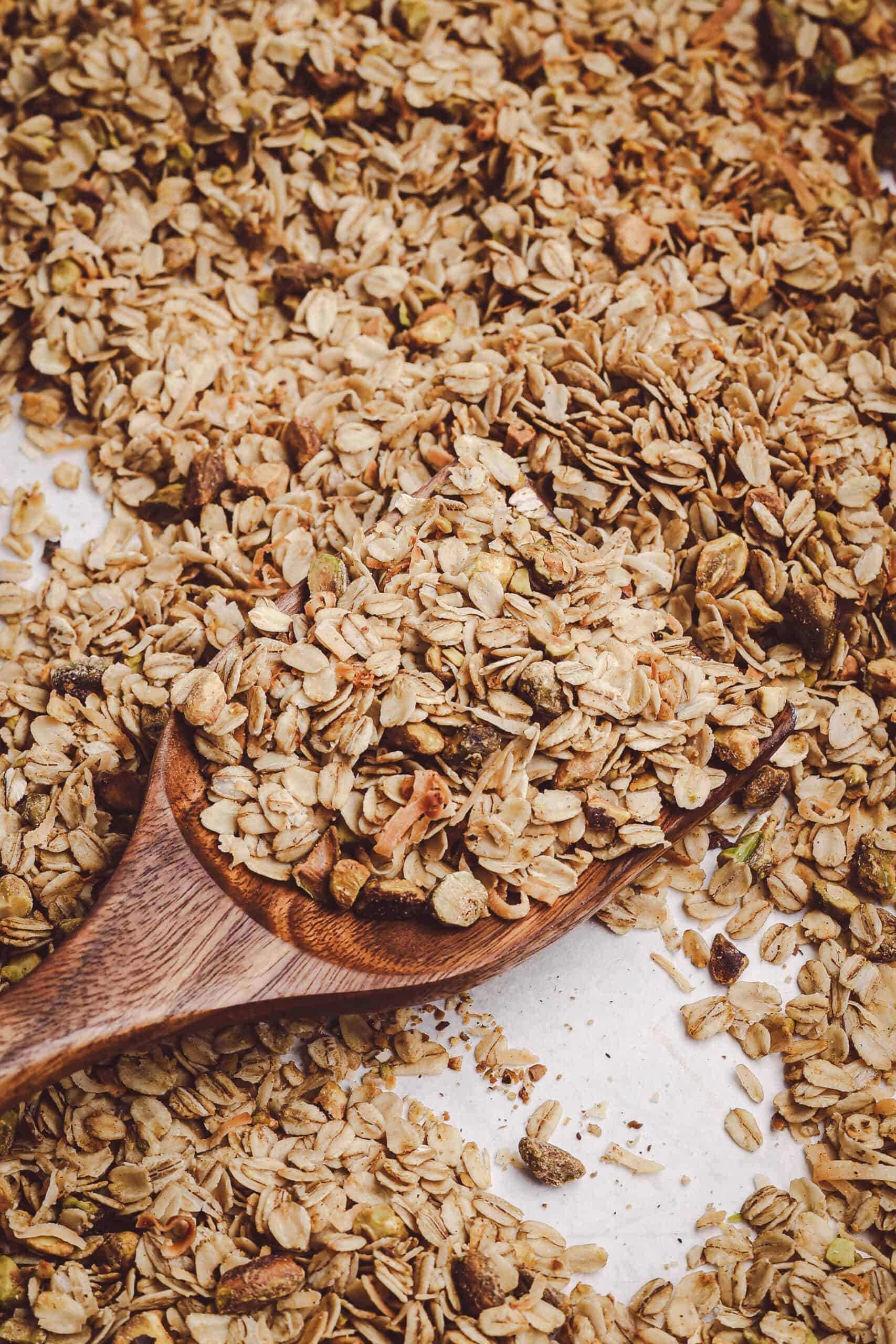Homemade granola with rolled oats, toasted coconut, and chopped nuts served on a wooden spoon with a golden, crisp texture.