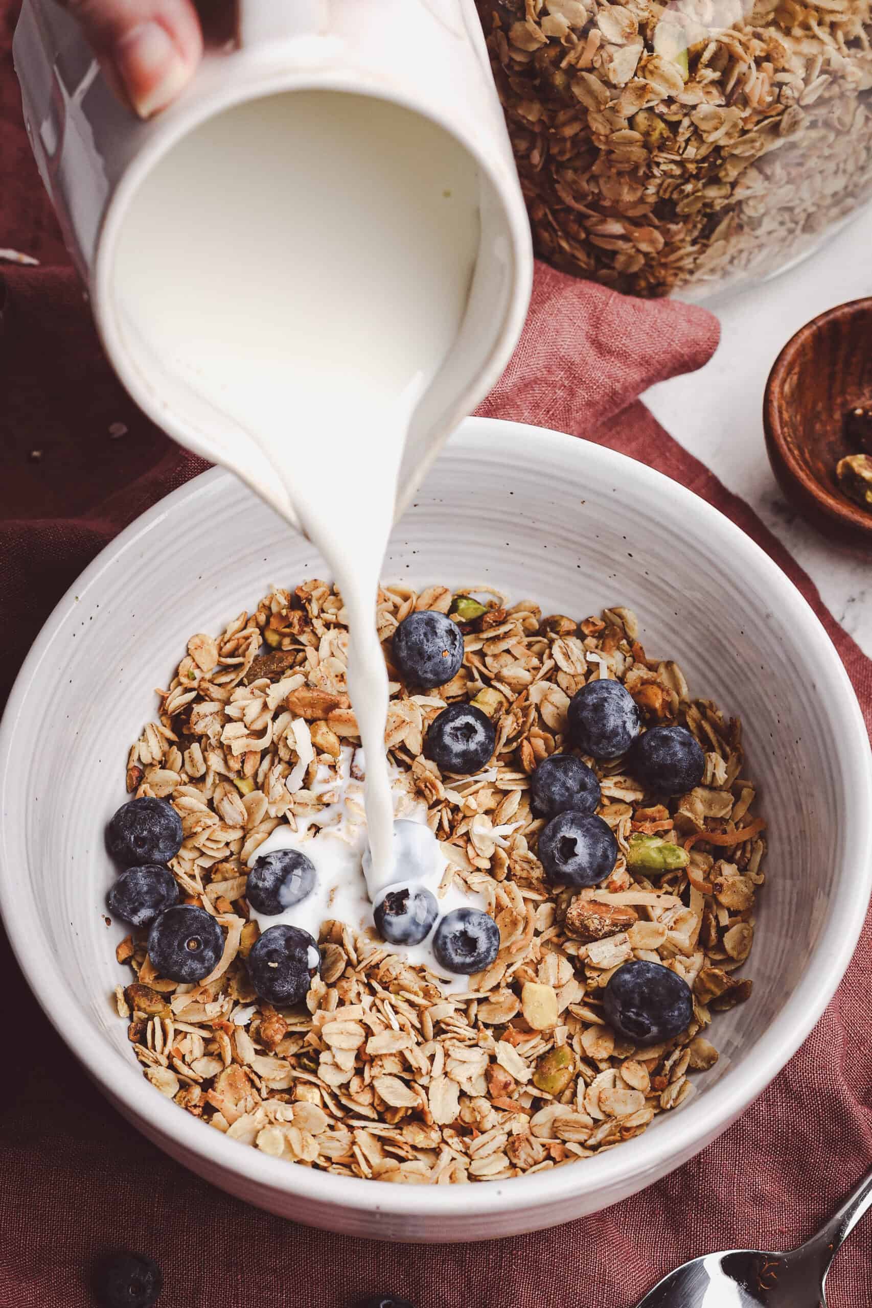 Homemade granola served in a bowl with fresh blueberries and milk being poured on top.