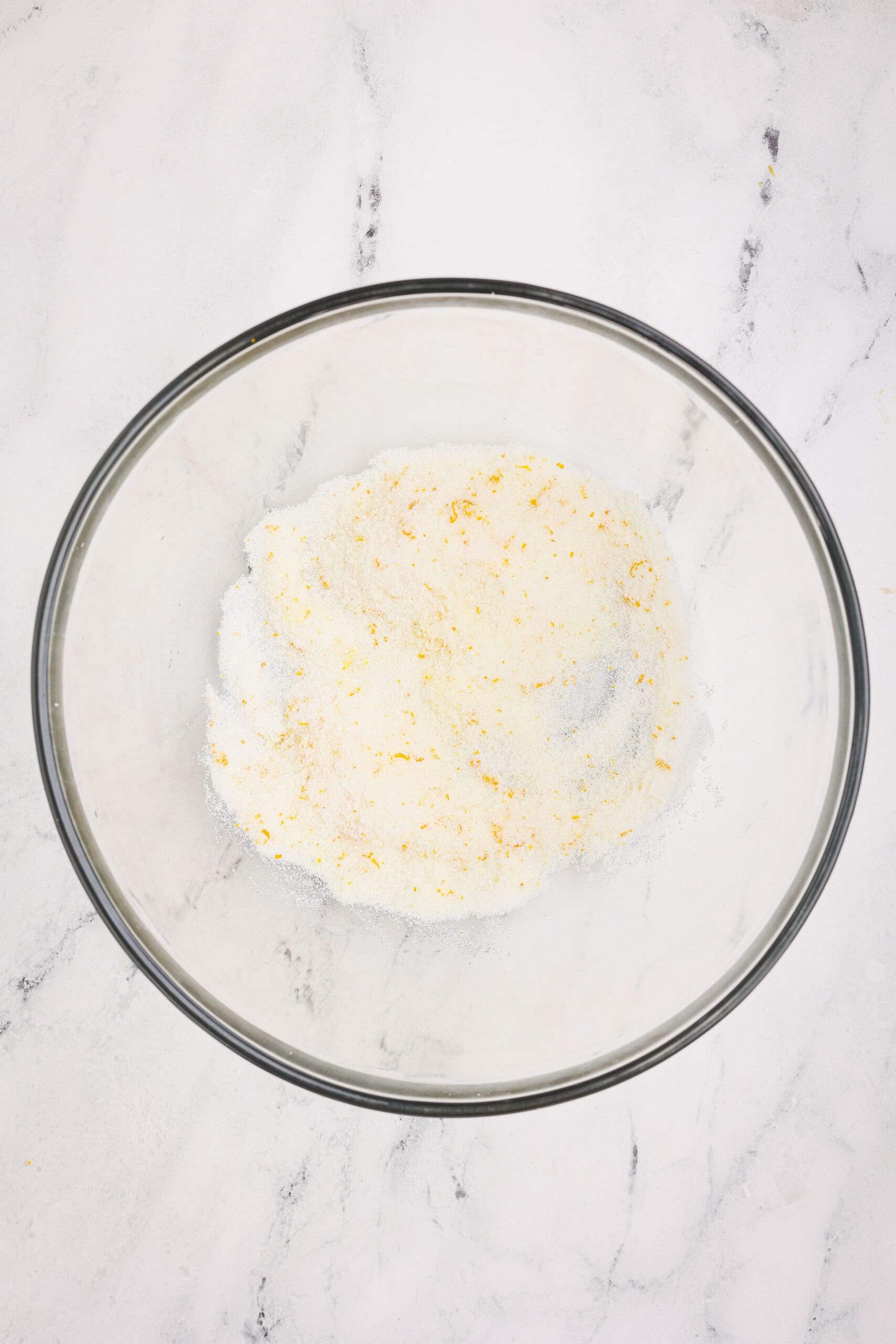 Granulated sugar mixed with orange zest in a glass bowl, showing bright citrus flecks.