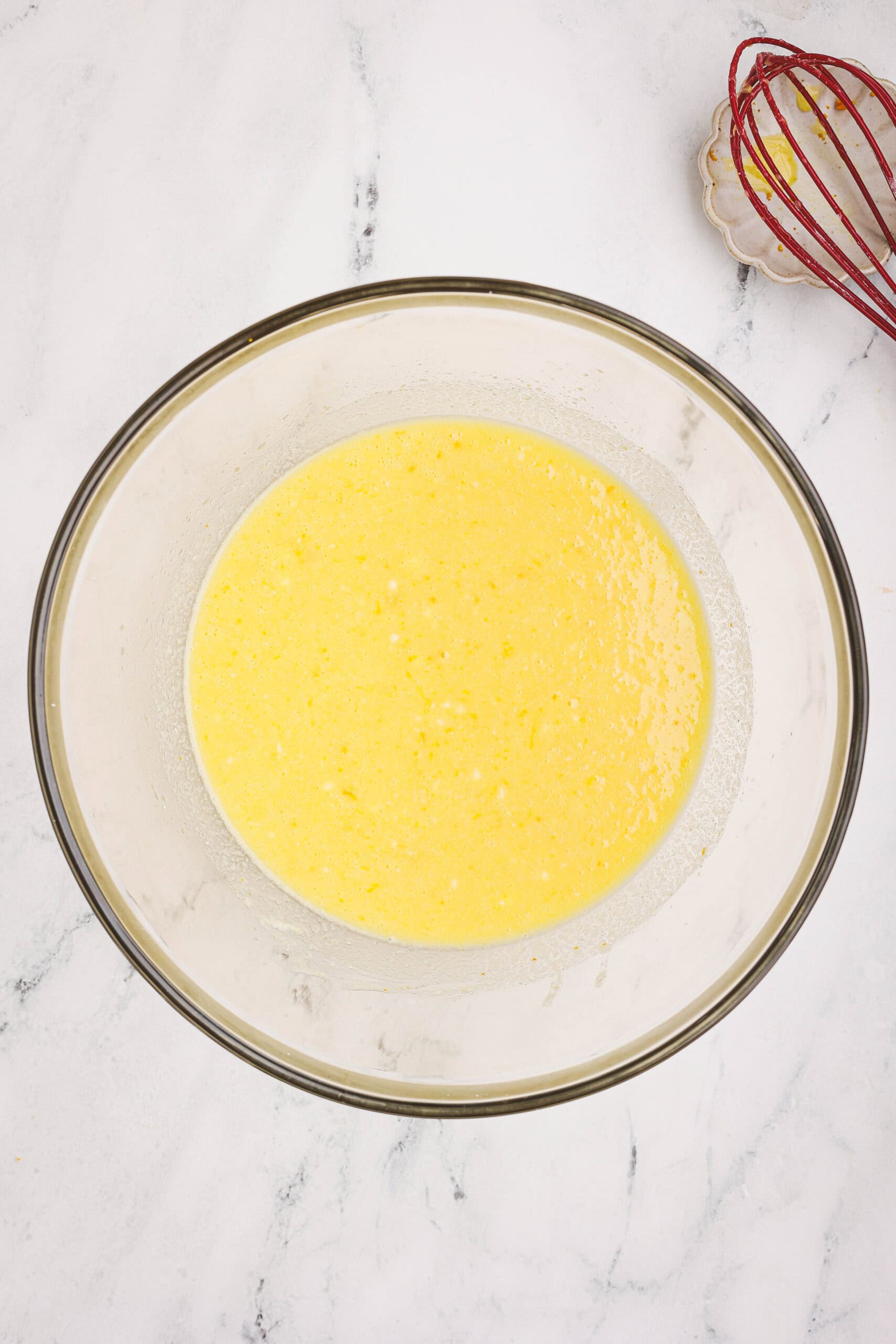 Wet ingredients for orange loaf batter combined in a bowl with a whisk nearby.