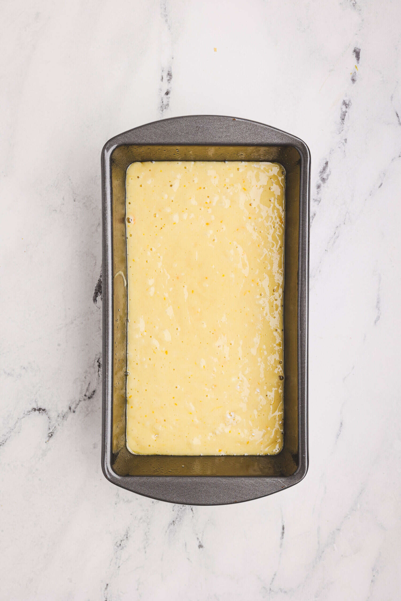 Orange loaf batter poured into a greased loaf pan, ready for baking.