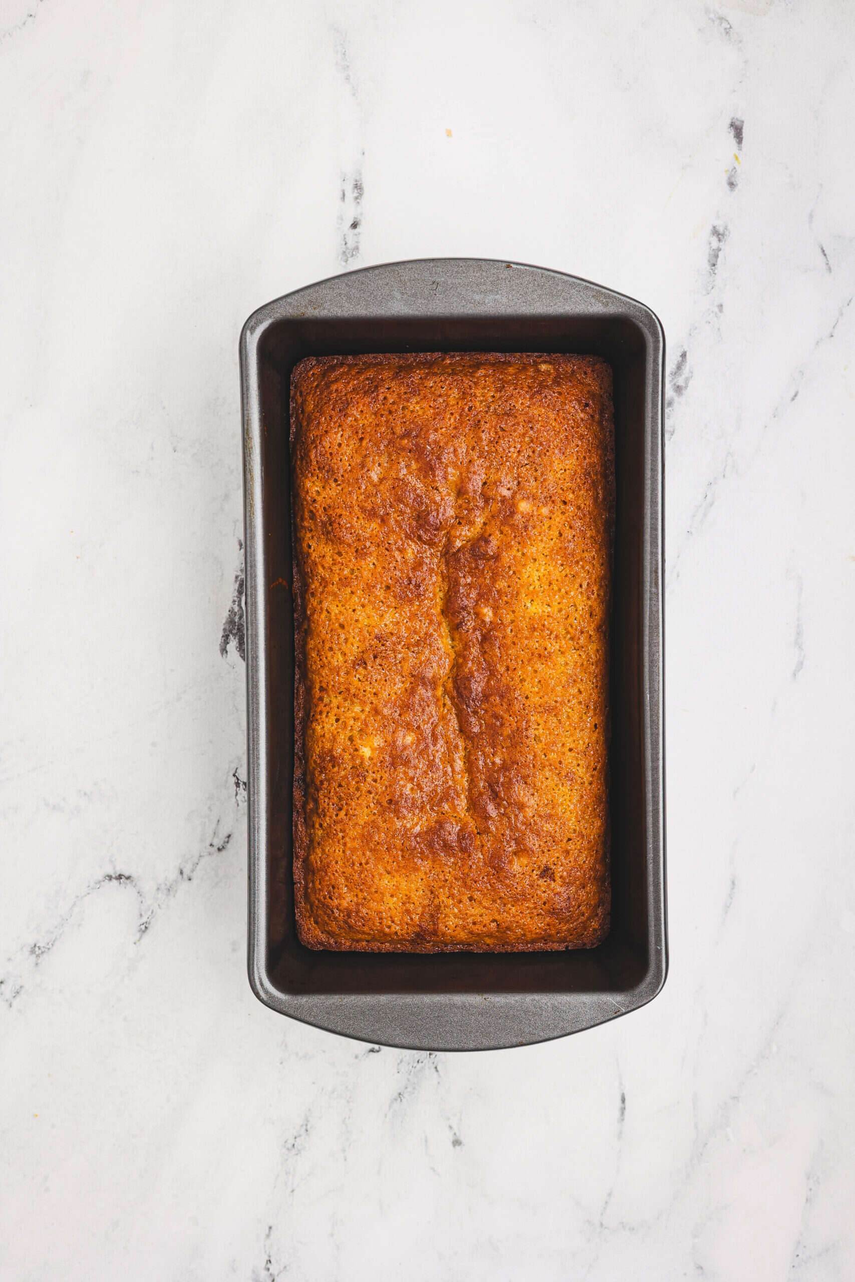 Freshly baked orange quick loaf in a metal loaf pan on a marble surface.