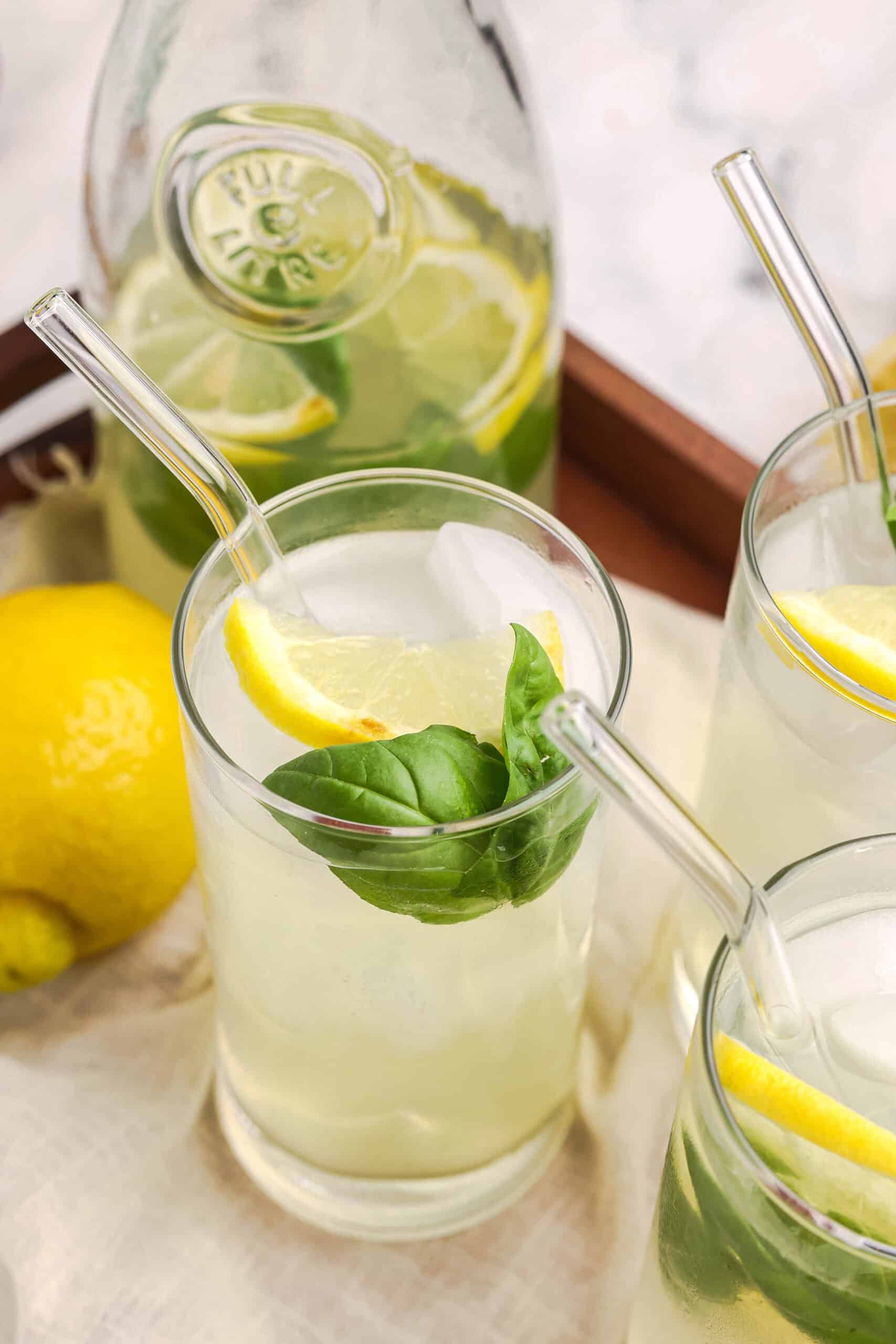 Close-up of basil lemonade in a glass with ice, lemon slice, and fresh basil garnish.