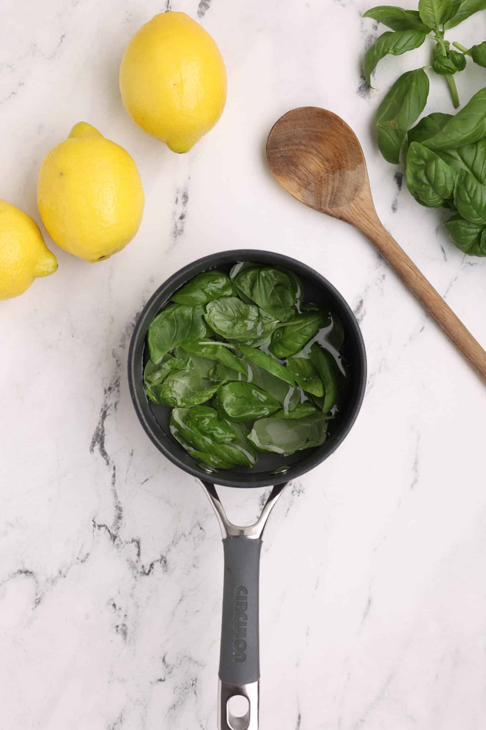 Basil leaves simmering in a saucepan with sugar and water to make basil simple syrup.