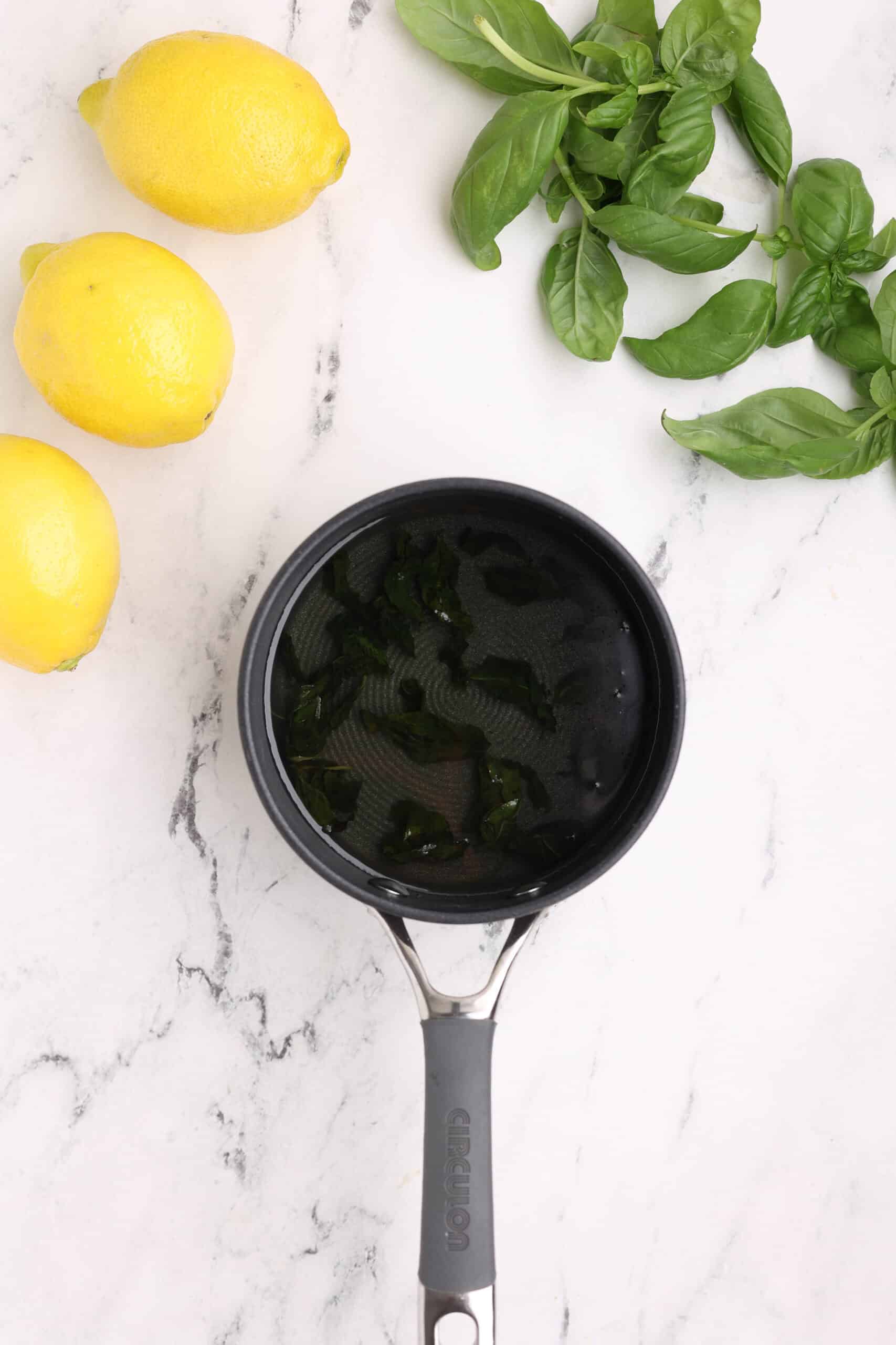 Darkened basil leaves steeping in hot syrup in a saucepan during basil lemonade preparation.