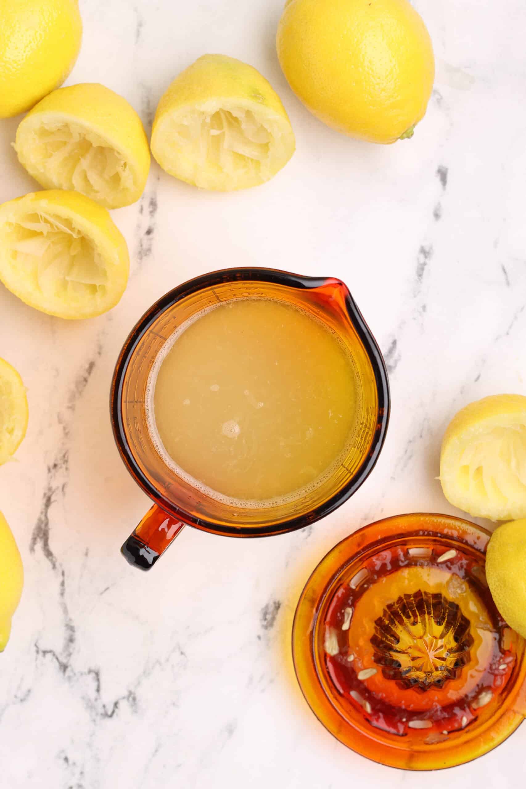 Freshly squeezed lemon juice in a measuring cup surrounded by juiced lemon halves.