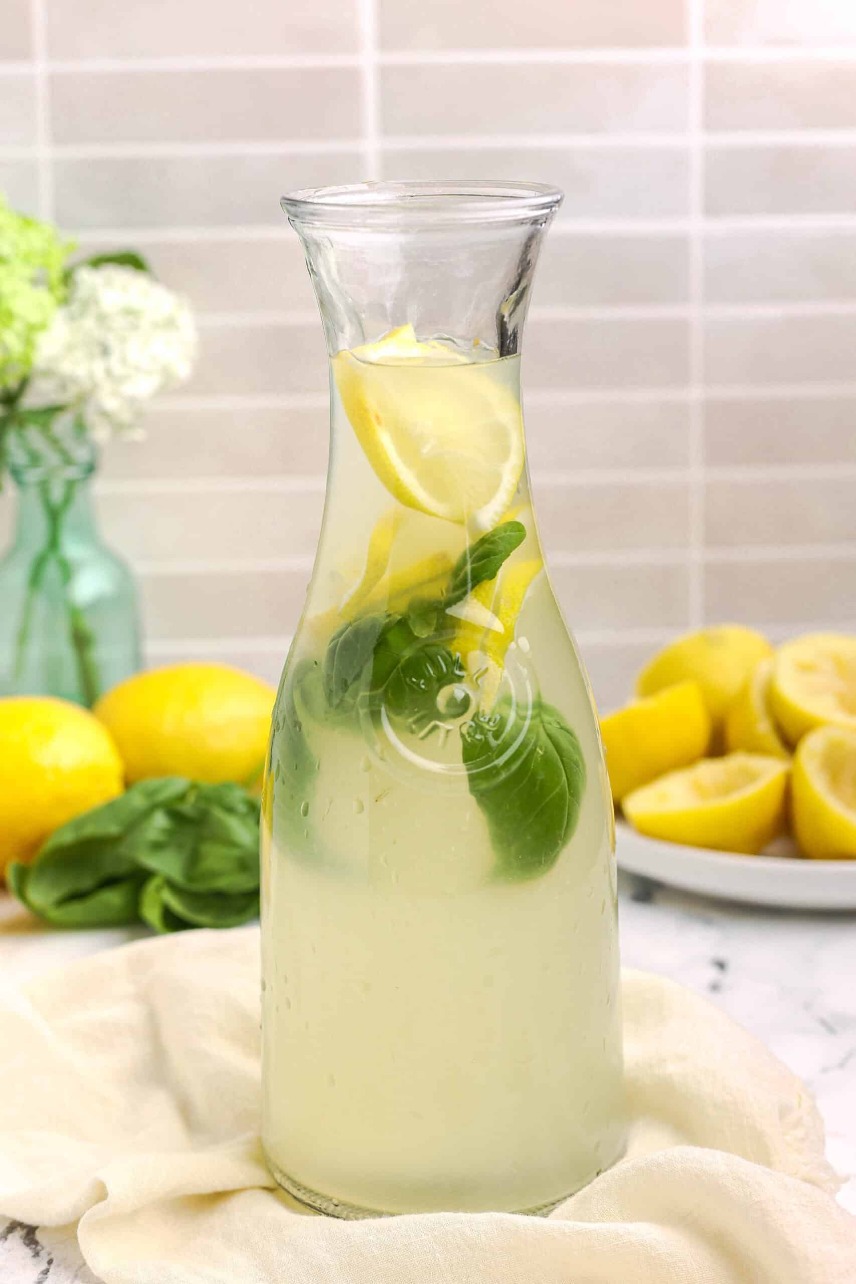 Glass pitcher filled with basil lemonade, lemon slices, and fresh basil leaves, ready to serve.