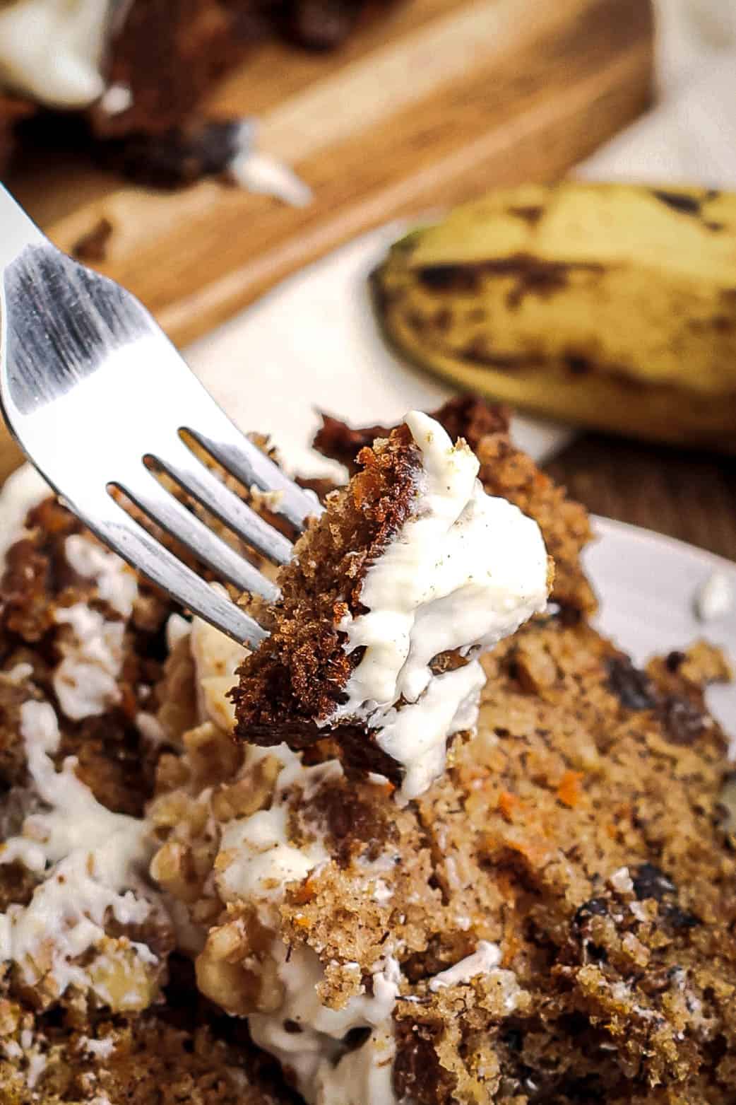 Fork lifting a bite of carrot cake banana bread with cream cheese frosting showing moist crumb texture