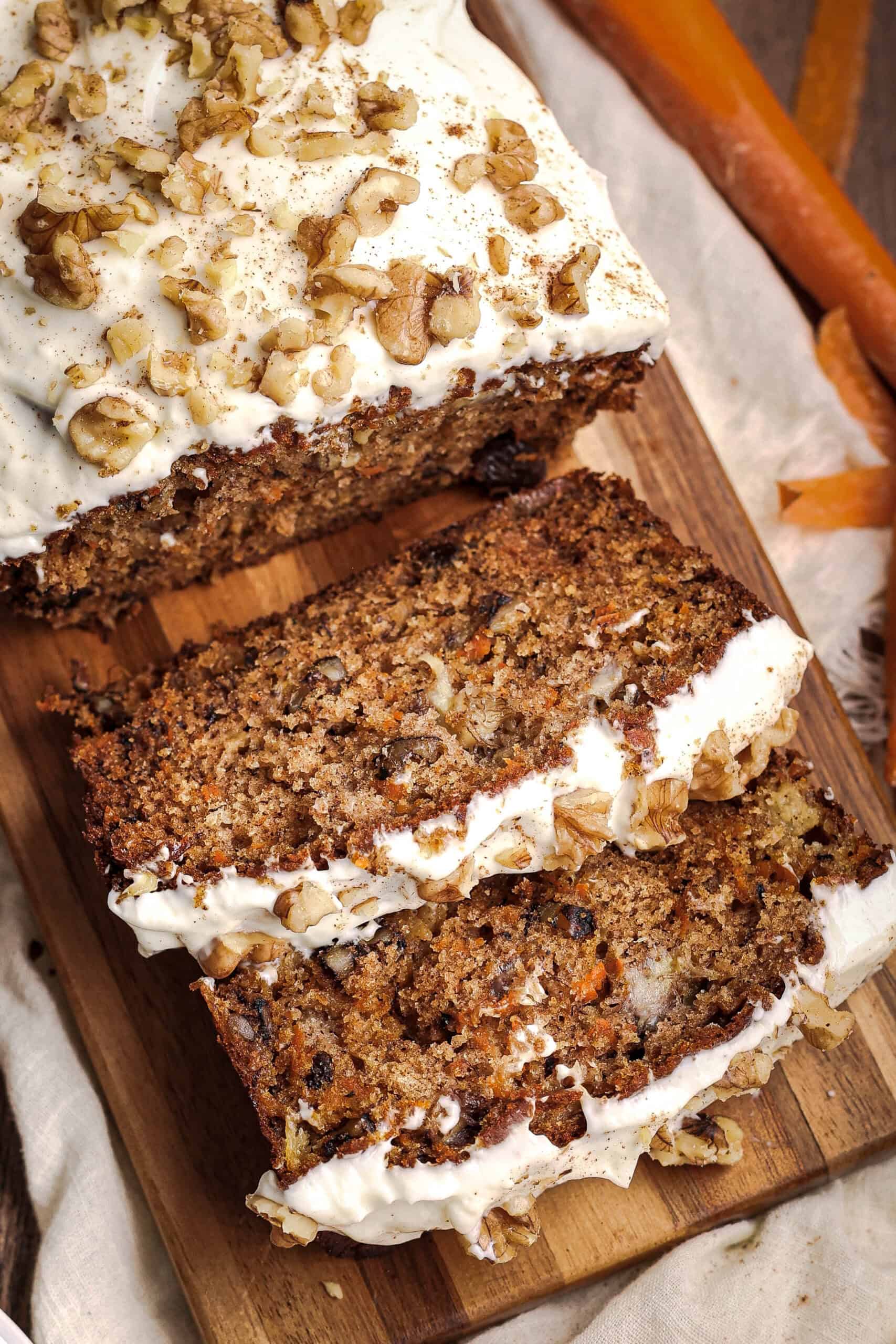 Carrot cake banana bread slices with cream cheese frosting and chopped walnuts on a wooden board