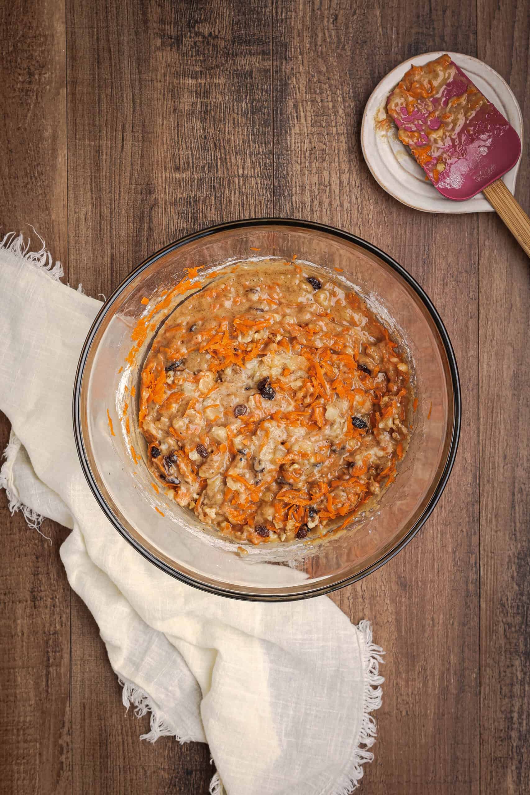 Carrot cake banana bread batter with grated carrots, raisins, and nuts being folded together