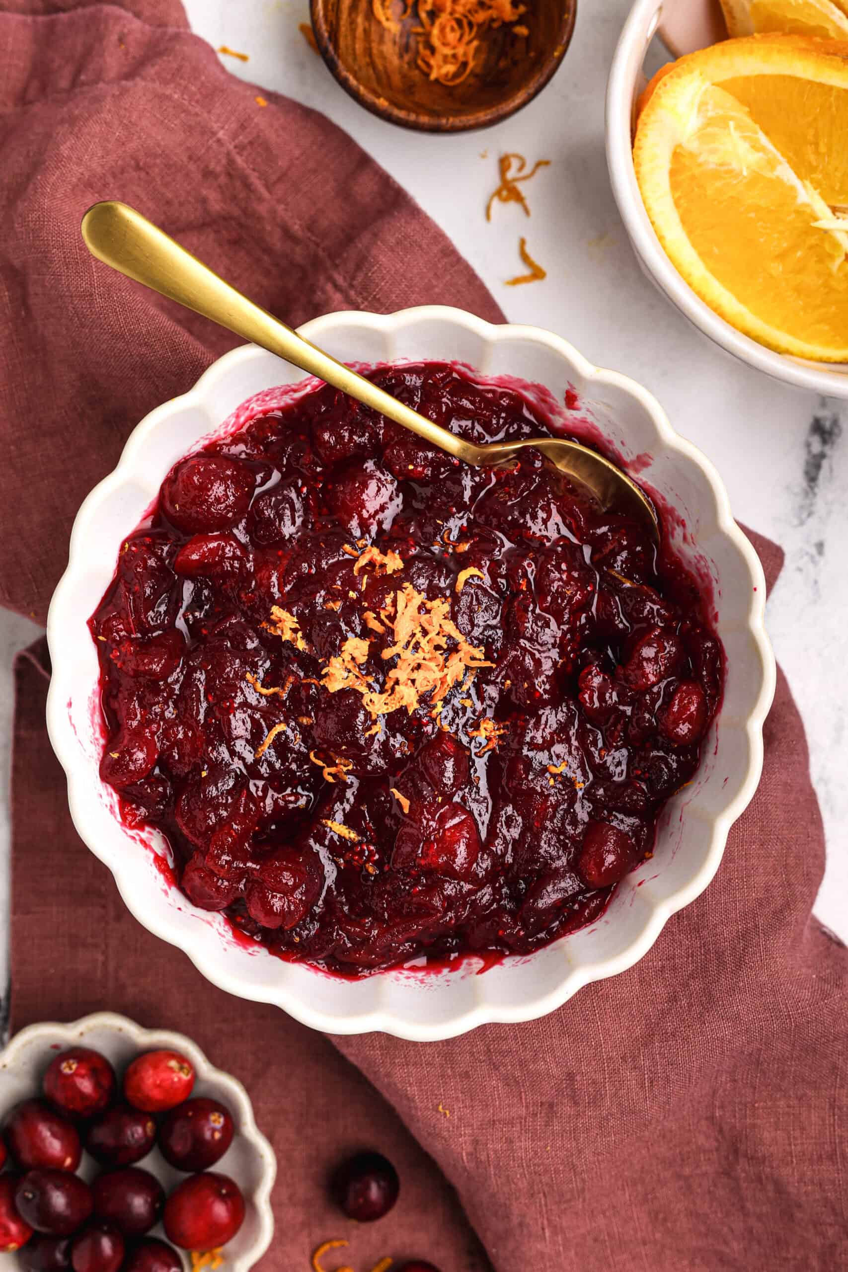Homemade cranberry orange sauce in a white bowl topped with fresh orange zest and served with a gold spoon.