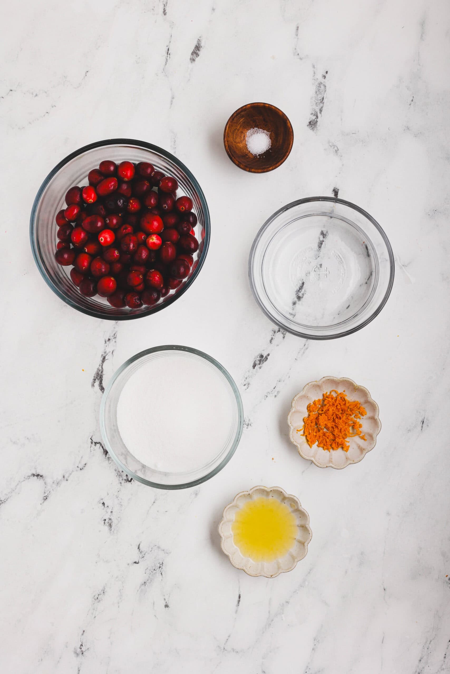 ngredients for cranberry orange sauce including fresh cranberries, sugar, water, orange zest, orange juice, and salt on a white surface.