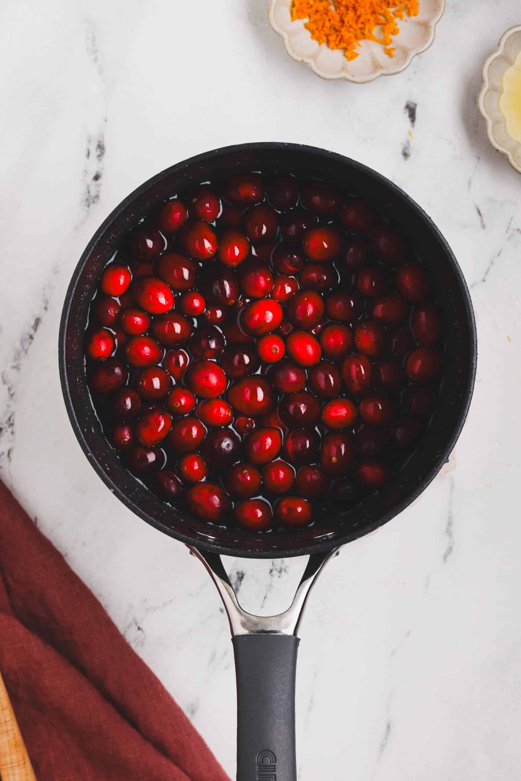 Fresh cranberries added to a saucepan with liquid, beginning the cooking process for cranberry sauce.