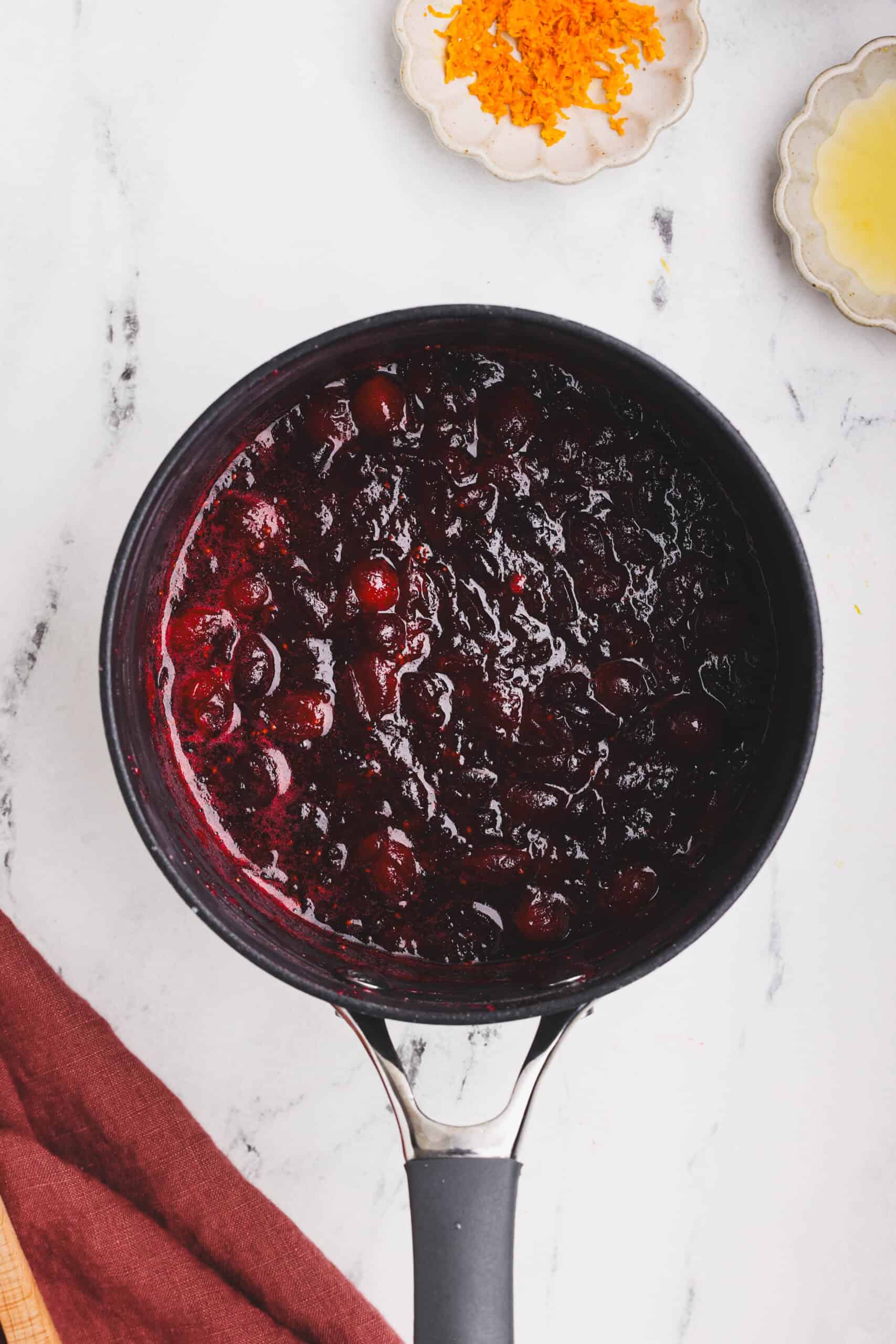 Cranberries simmering and breaking down into a thick cranberry sauce in a saucepan.