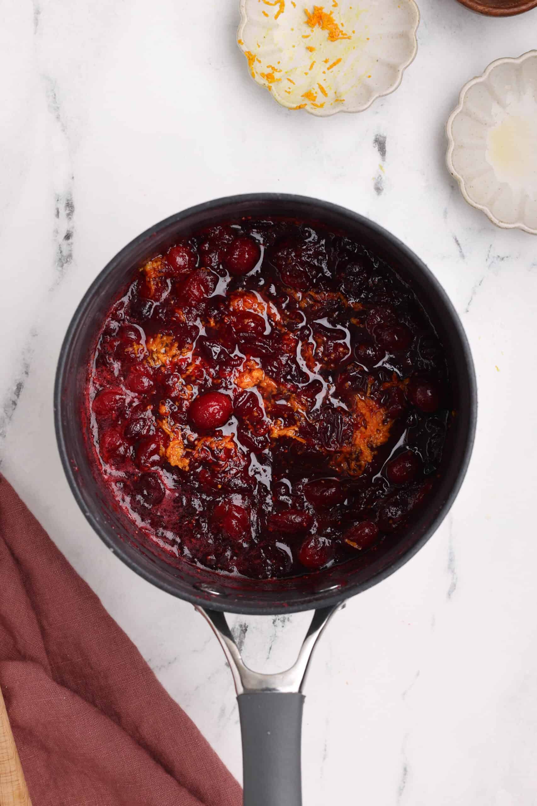 Cranberry orange sauce finished in a saucepan with orange zest mixed in for added citrus flavor.