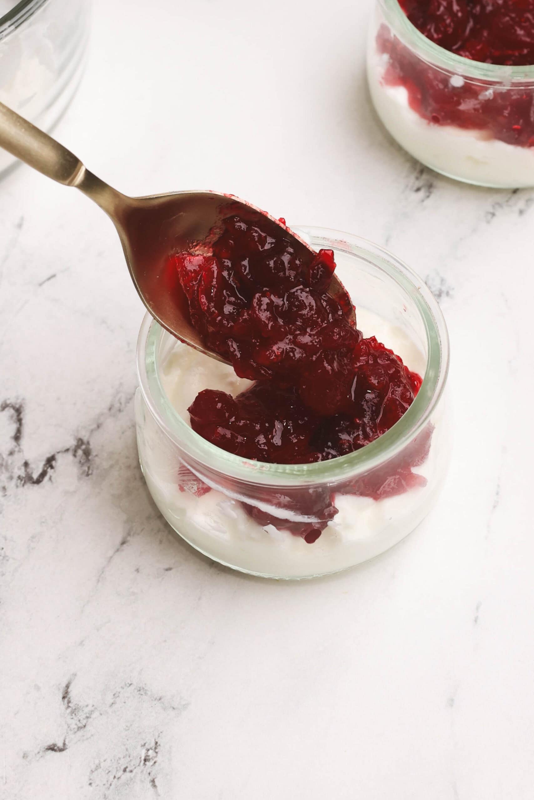 Layering cranberry orange sauce into a jar with a spoon over the yogurt layer.