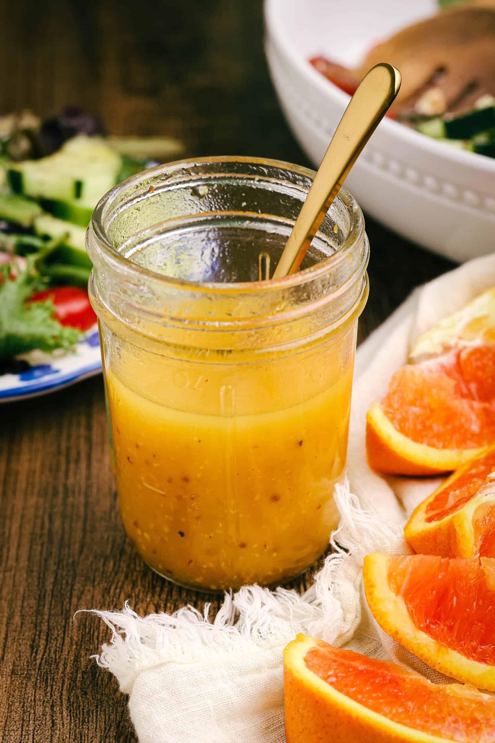 Jar of homemade citrus dressing styled with fresh grapefruit slices and salad ingredients in the background.