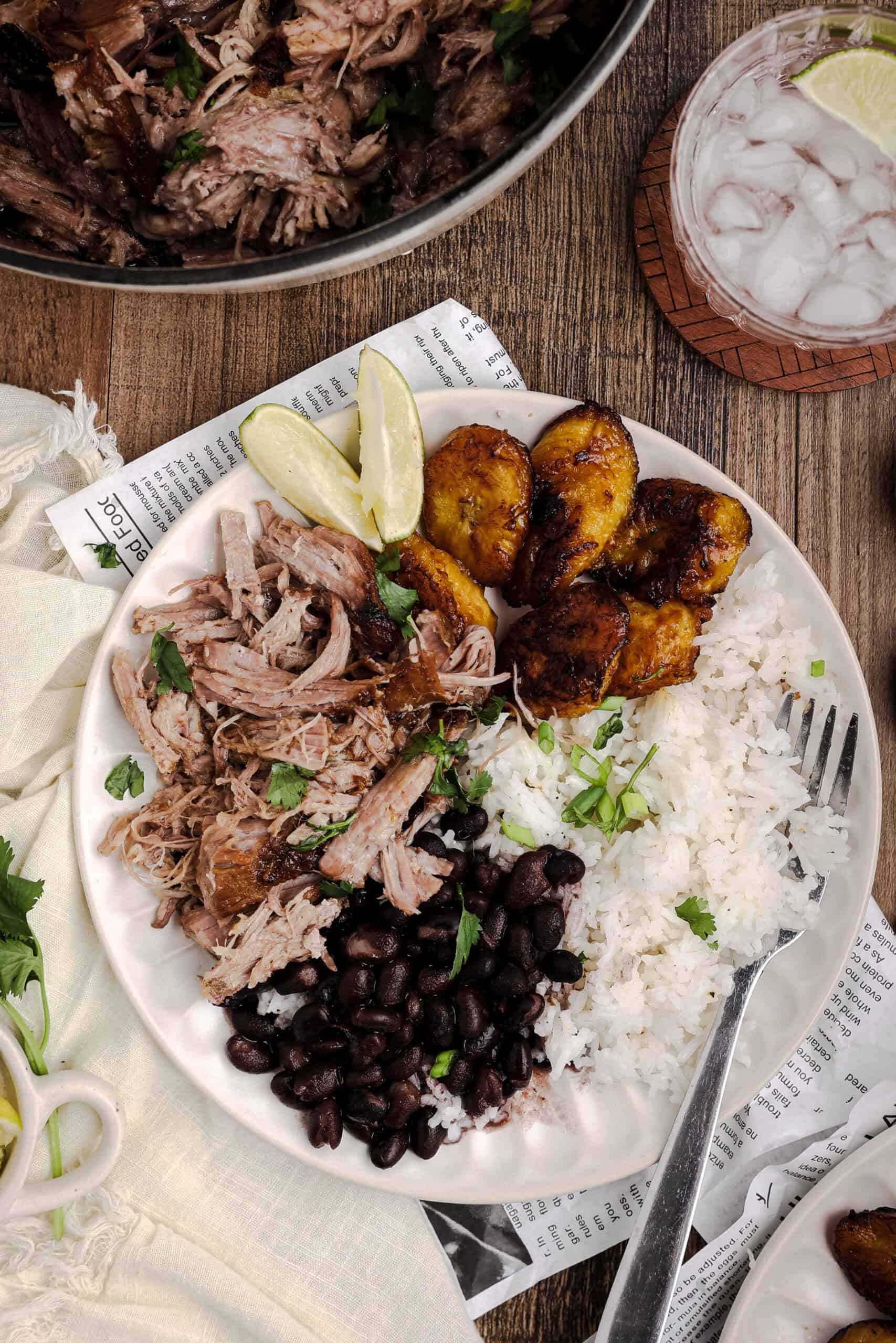 Plate of Cuban mojo pork roast served with black beans, white rice, fried sweet plantains, and fresh lime wedges.