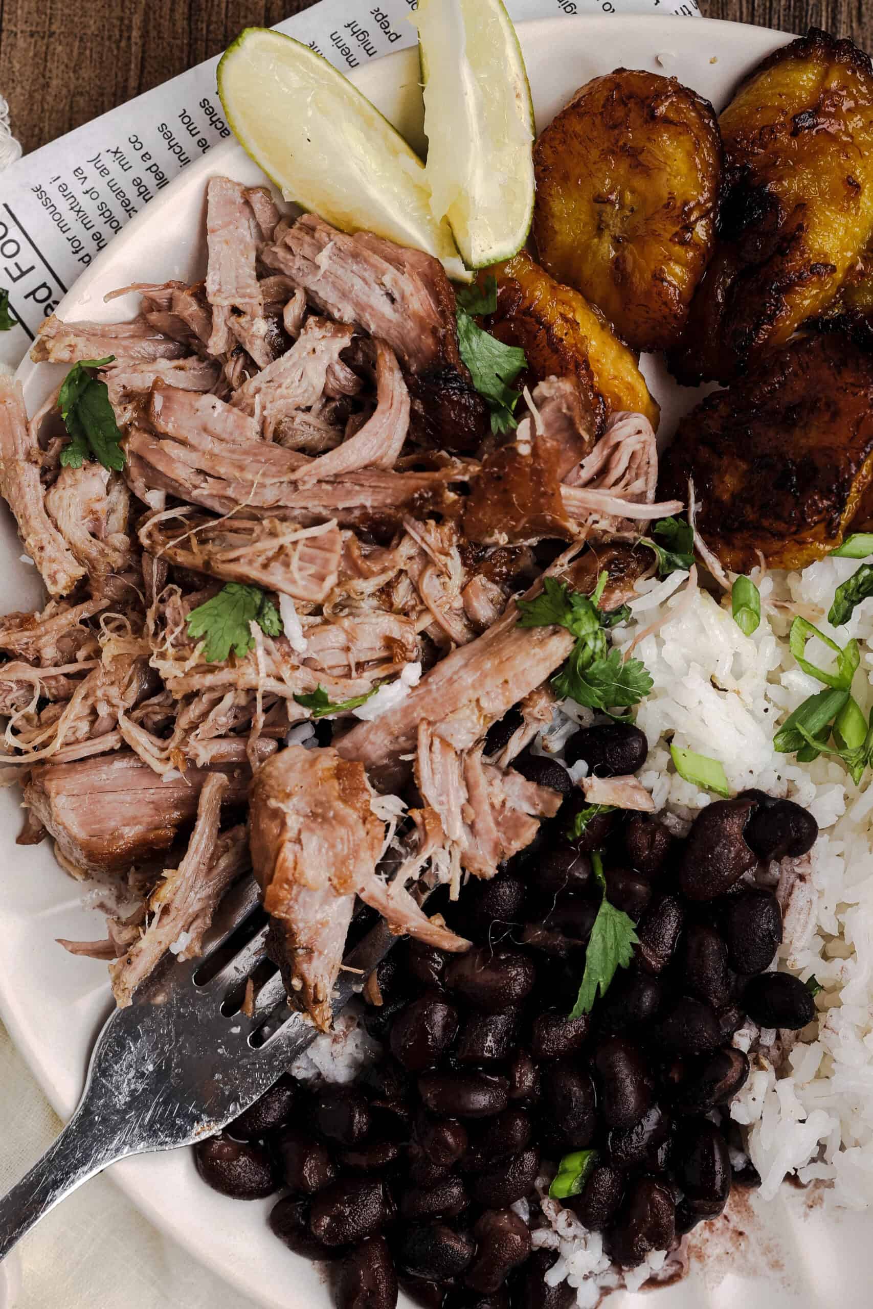 Close-up of authentic mojo pork served with Cuban black beans, white rice, and caramelized sweet plantains.